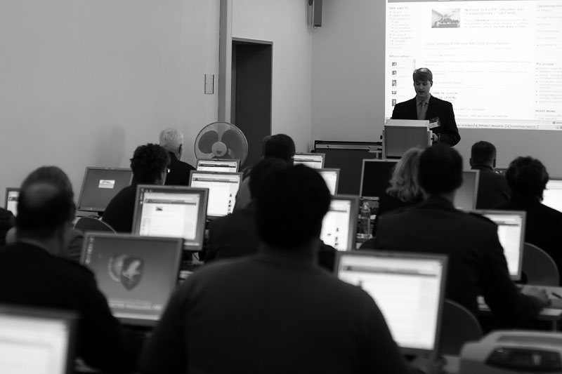 A presenter leads a Drupal training session in a computer lab with participants following along on their screens.