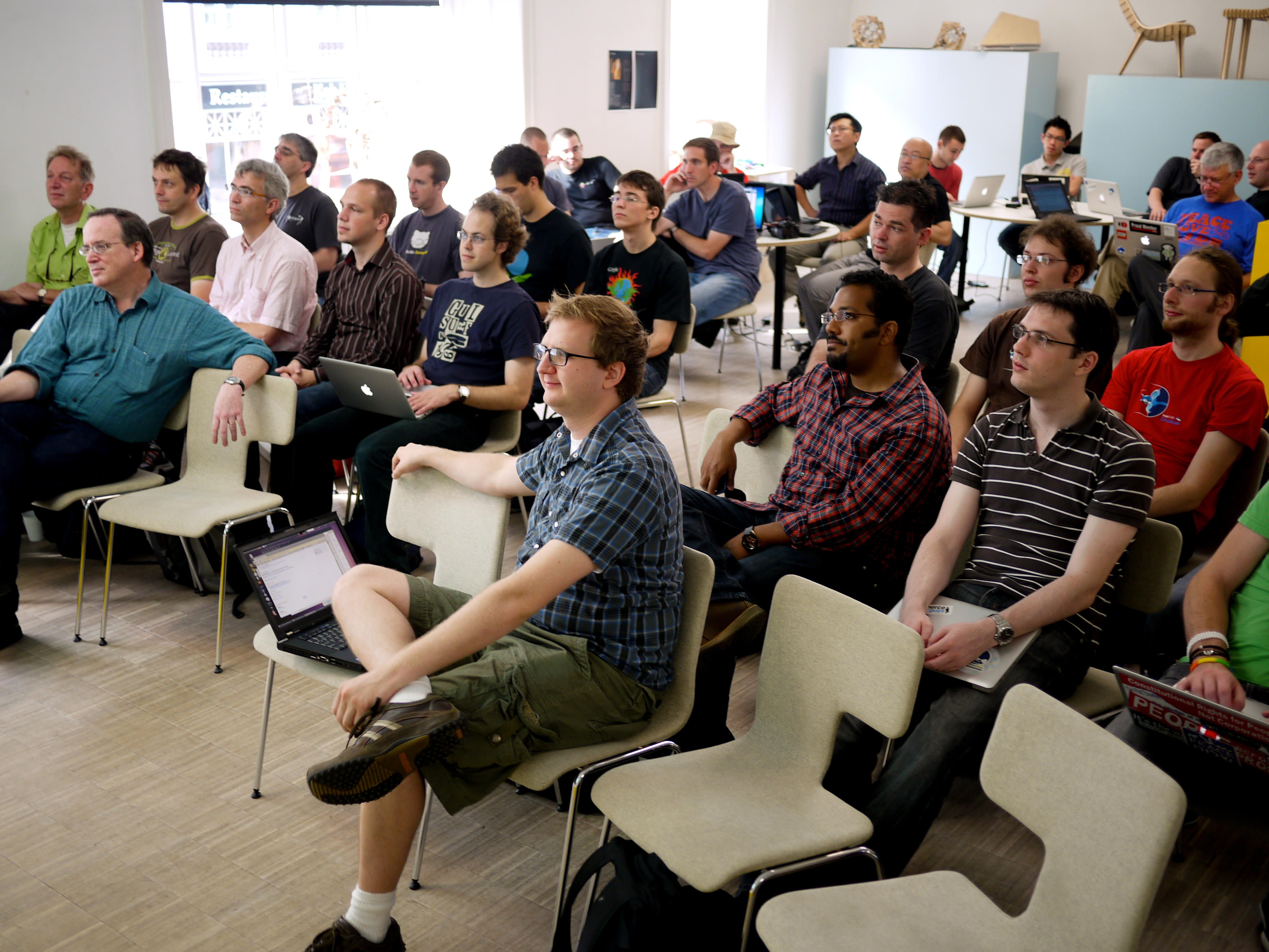 A group of people attentively listen during a DrupalCon Copenhagen 2010 code sprint, with laptops open.