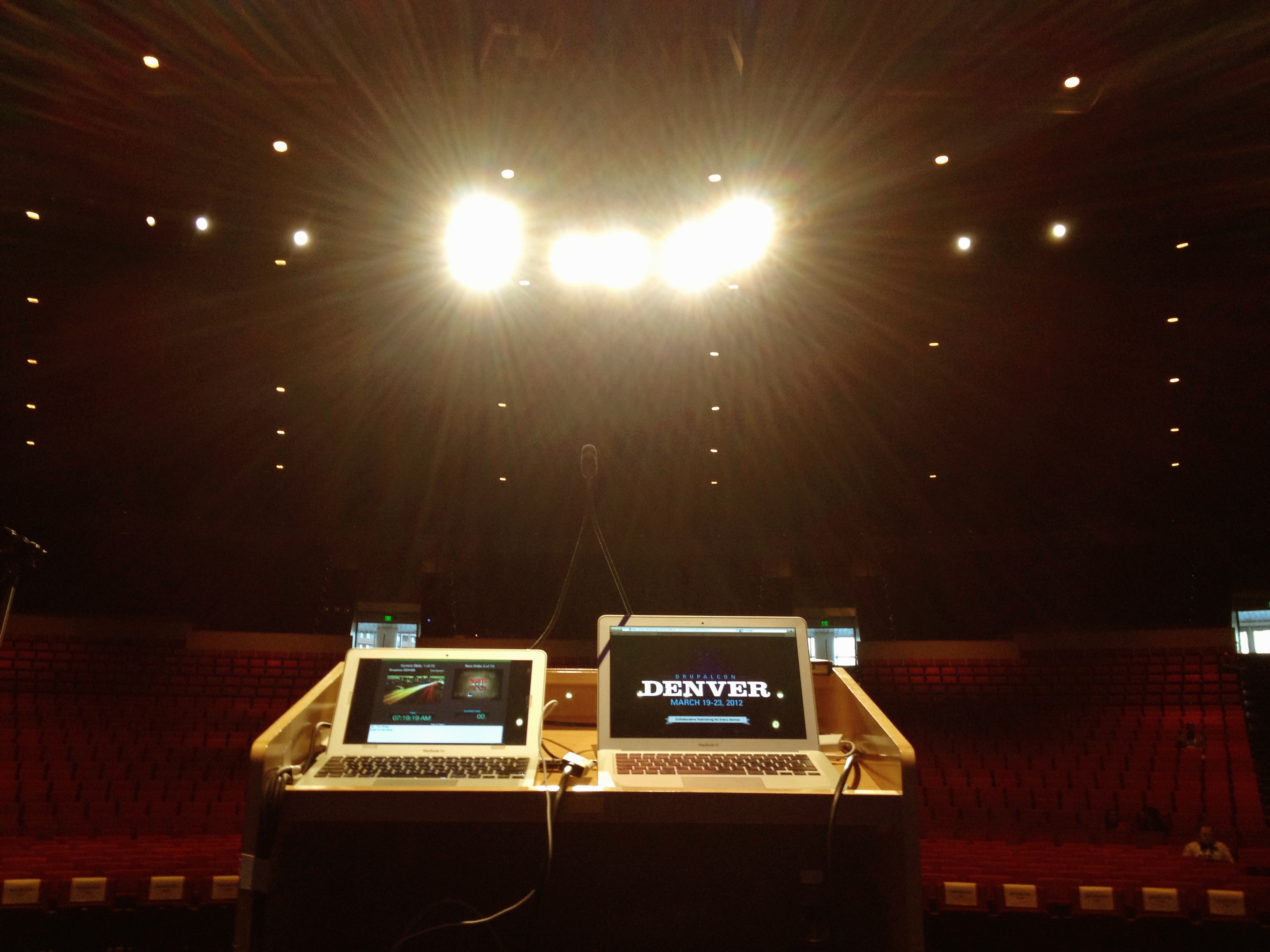 View from a keynote speaker's podium with two laptops displaying DrupalCon Denver 2012 content in a large auditorium.