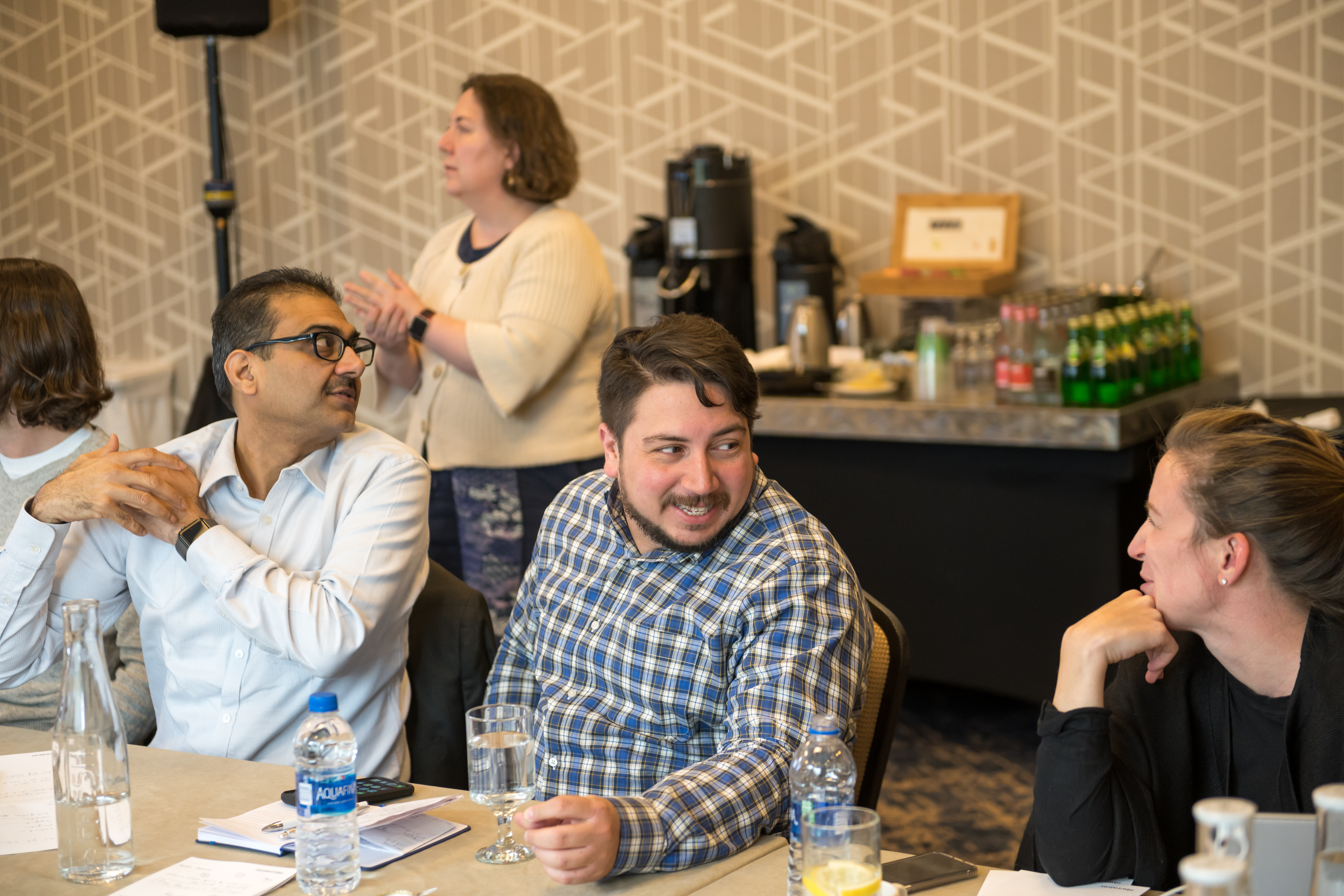 A group of people sit at a table, talking and listening.