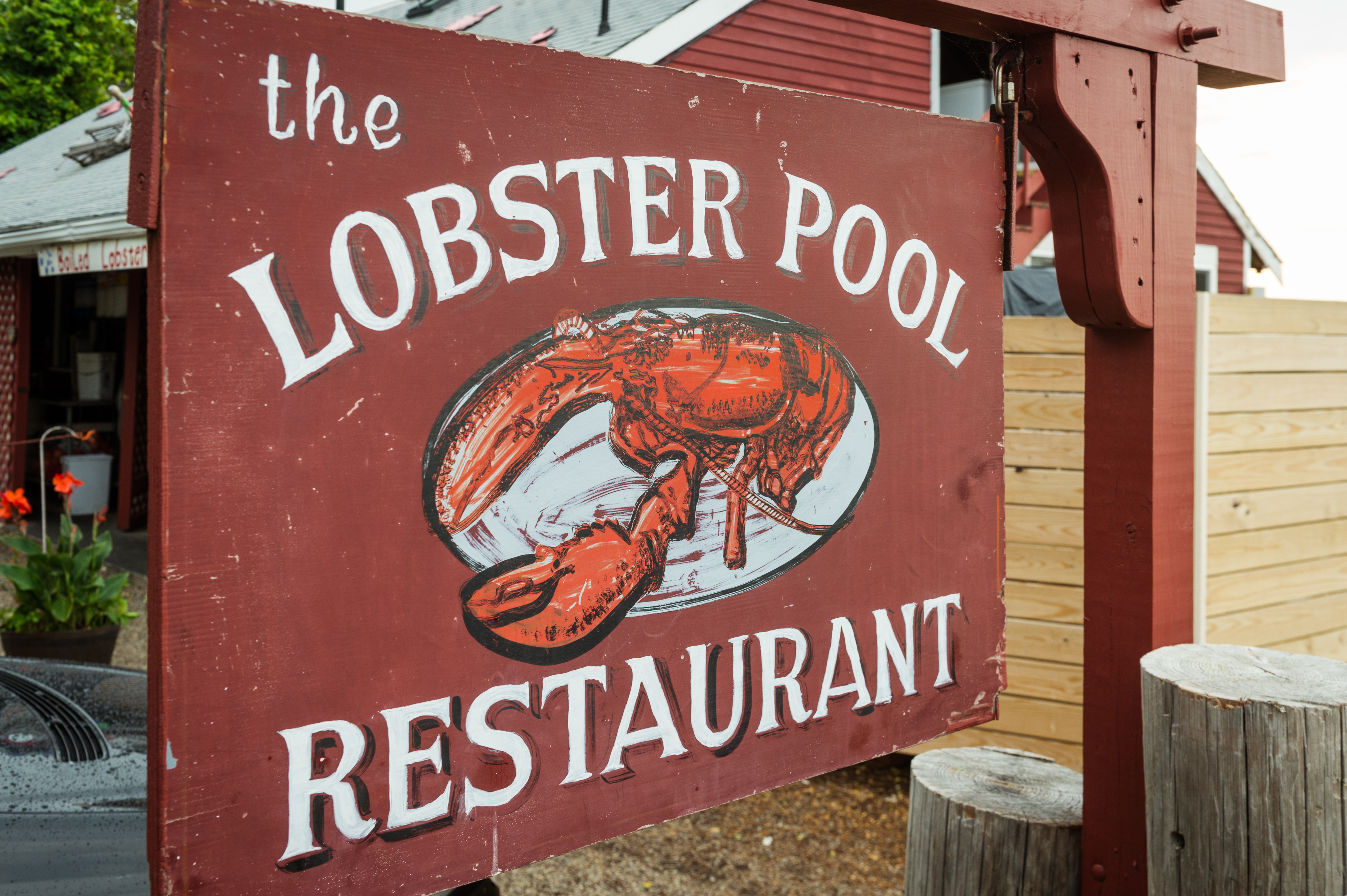 A red wooden sign for "The Lobster Pool Restaurant" with a painted lobster illustration, outside a rustic building.