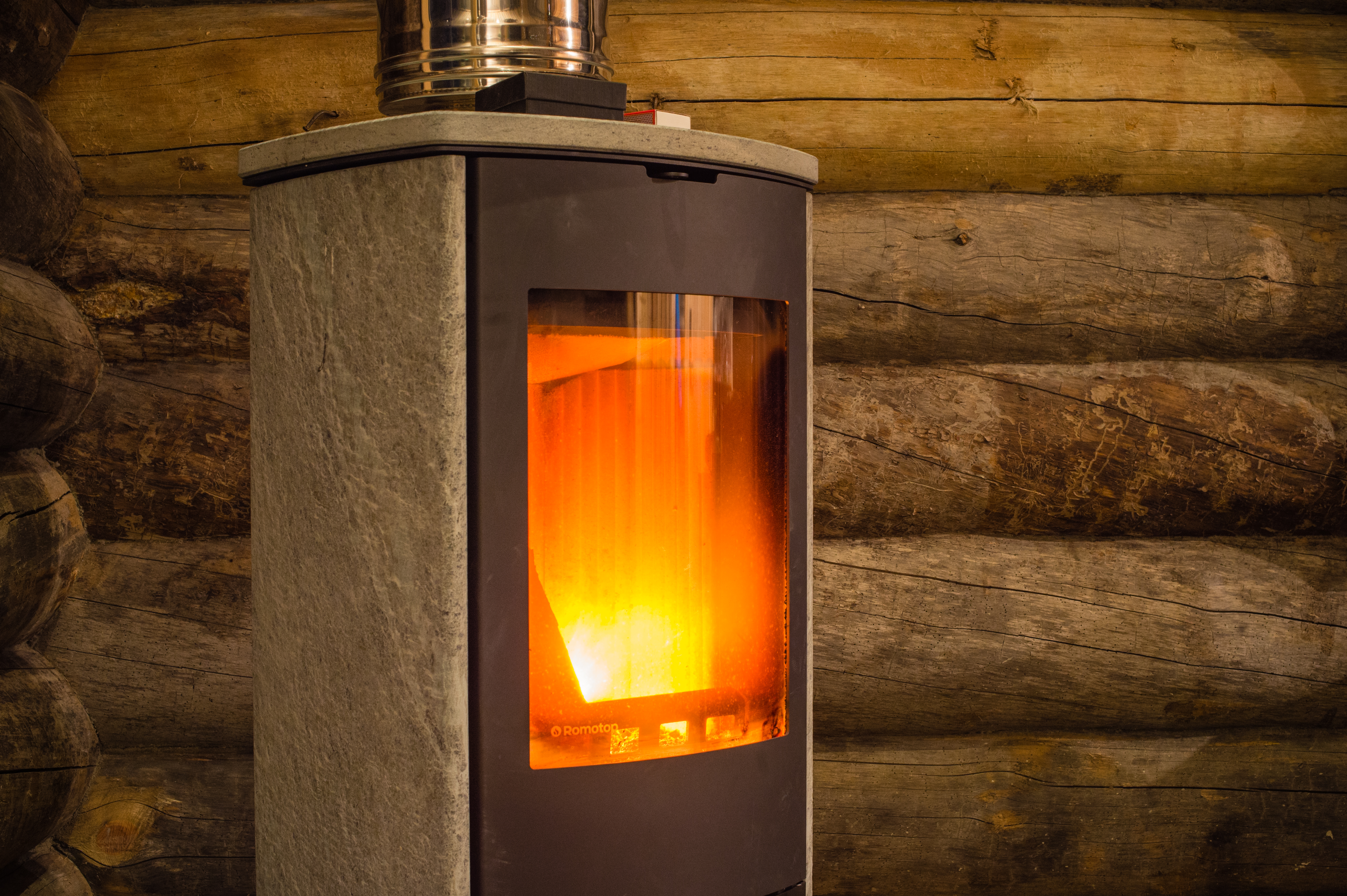 A wood-burning fireplace with a glass door showing a bright fire inside, set against a log cabin wall.