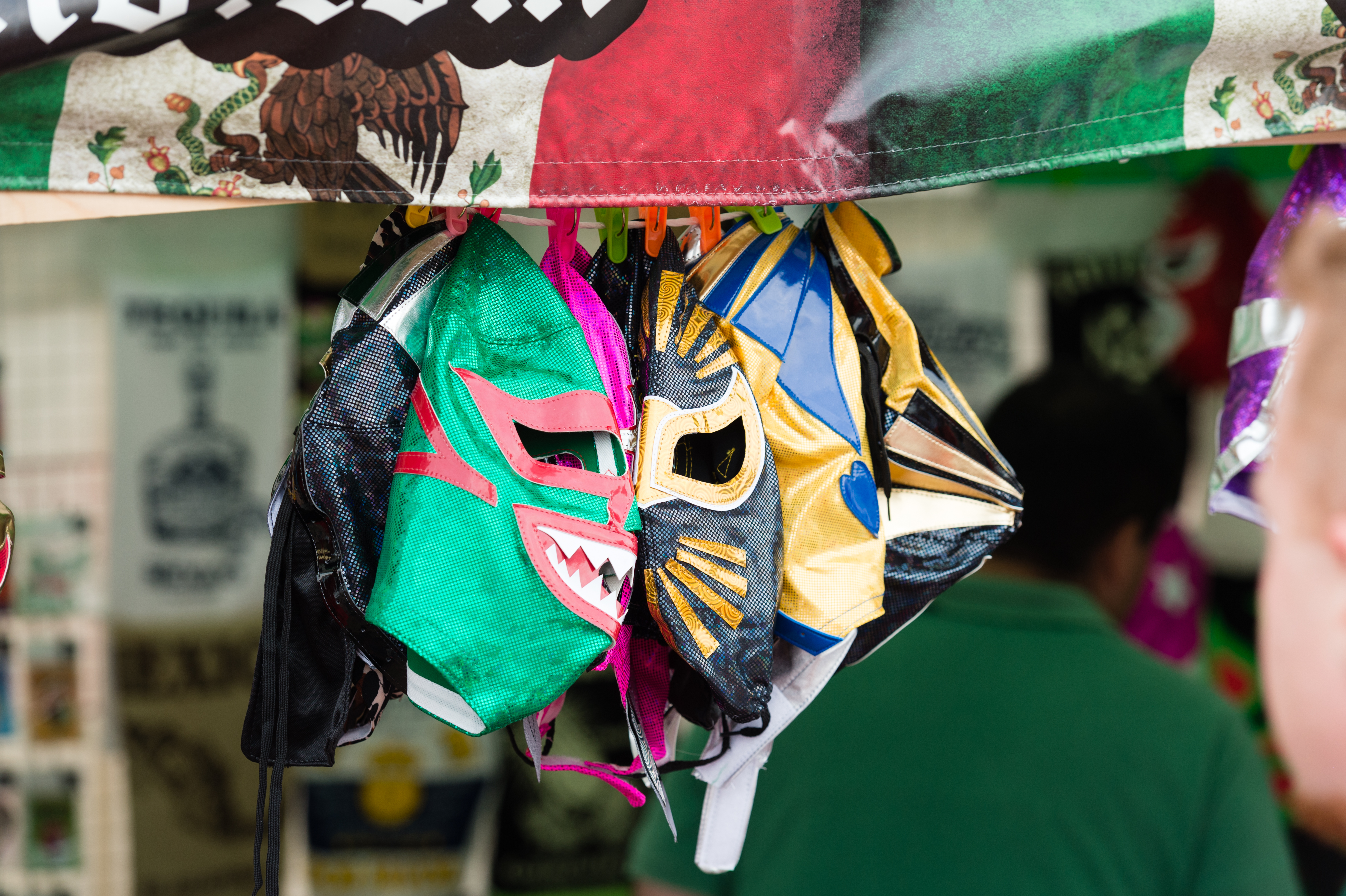 Colorful lucha libre masks hang from a stall, with people browsing in the background.