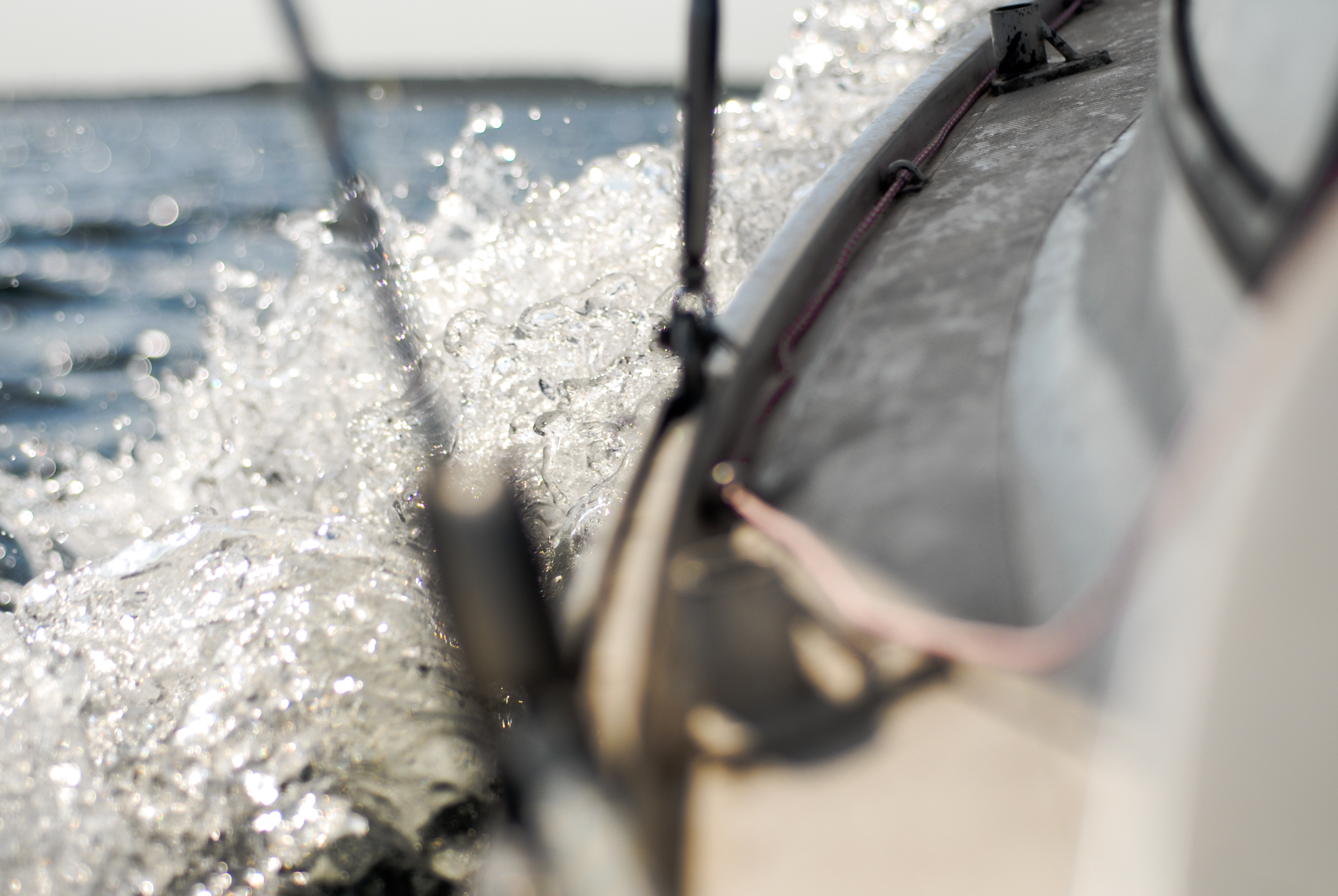 Water splashes against the side of a sailing boat, with ropes and rigging visible in the foreground.