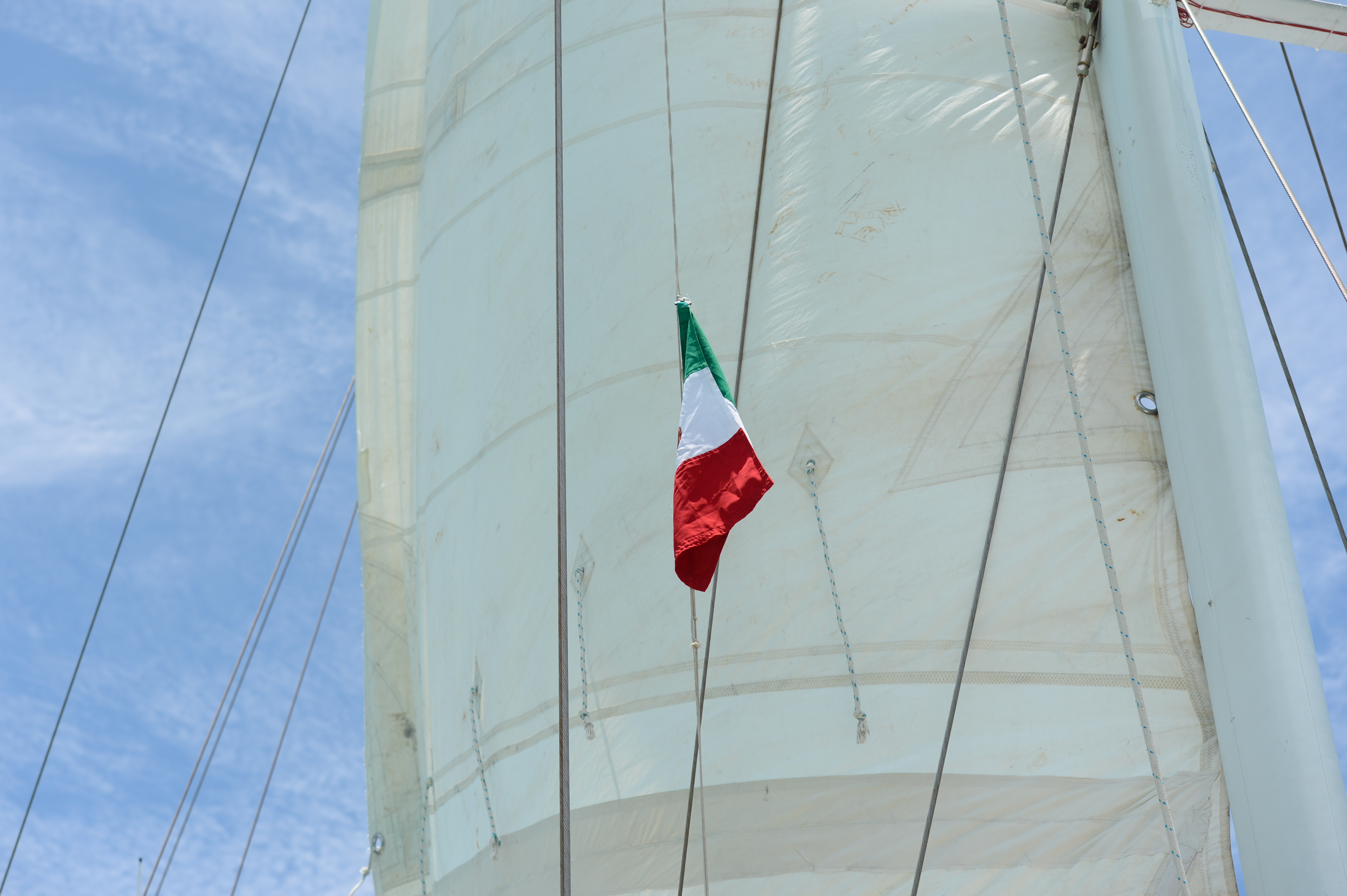 A Mexican flag hangs from the mast of a sailboat against a clear blue sky.