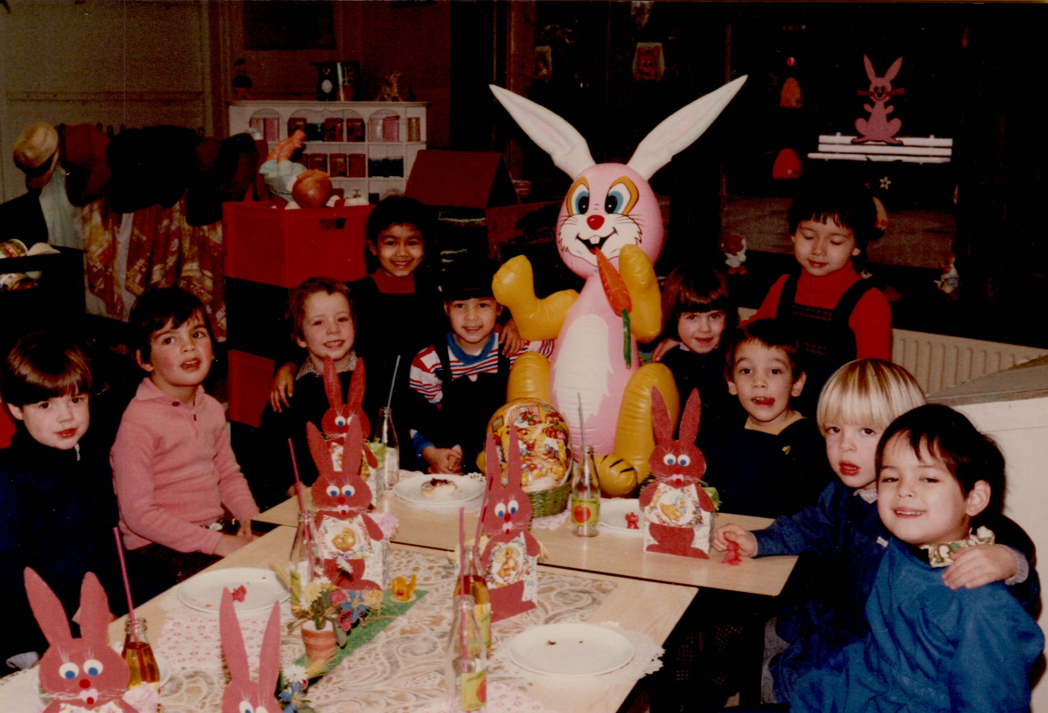 Children sit around a decorated table with bunny crafts and an inflatable rabbit, smiling and enjoying a festive party.