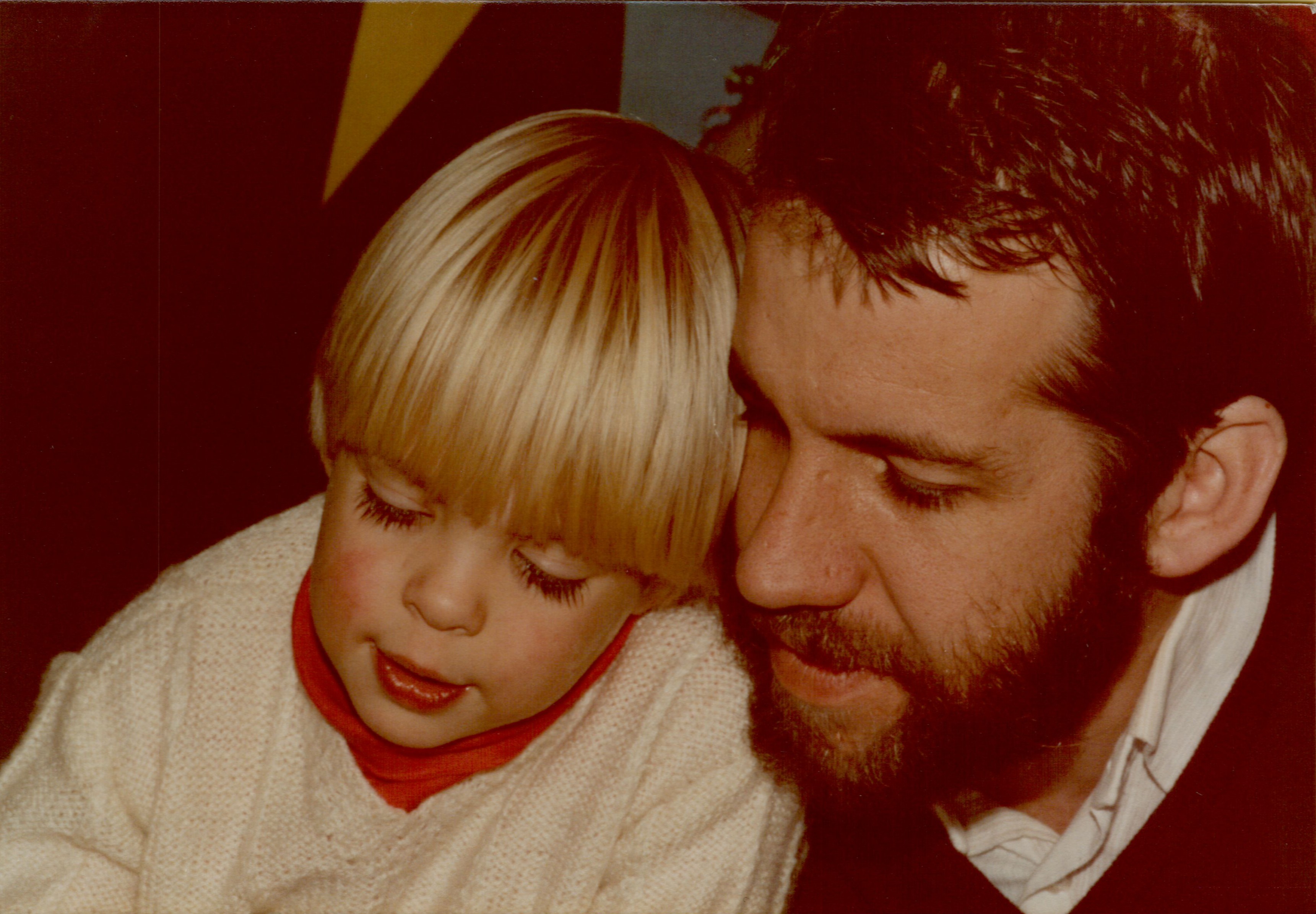 A young child and their father sit closely together, both looking down at something with focused expressions.