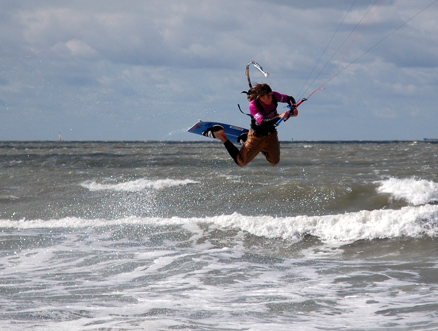 A person kiteboarding jumps above ocean waves while holding onto the control bar.