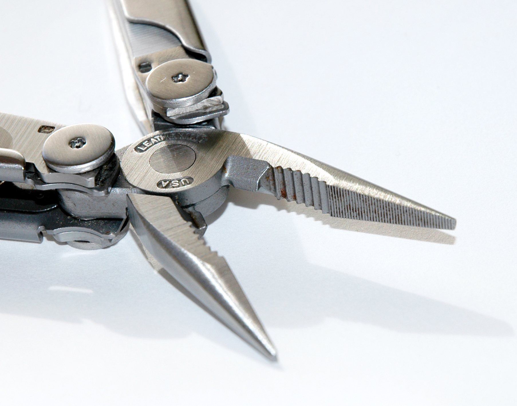 A close-up of a Leatherman multi-tool with its pliers open, showing metal details and slight rust on the jaws.