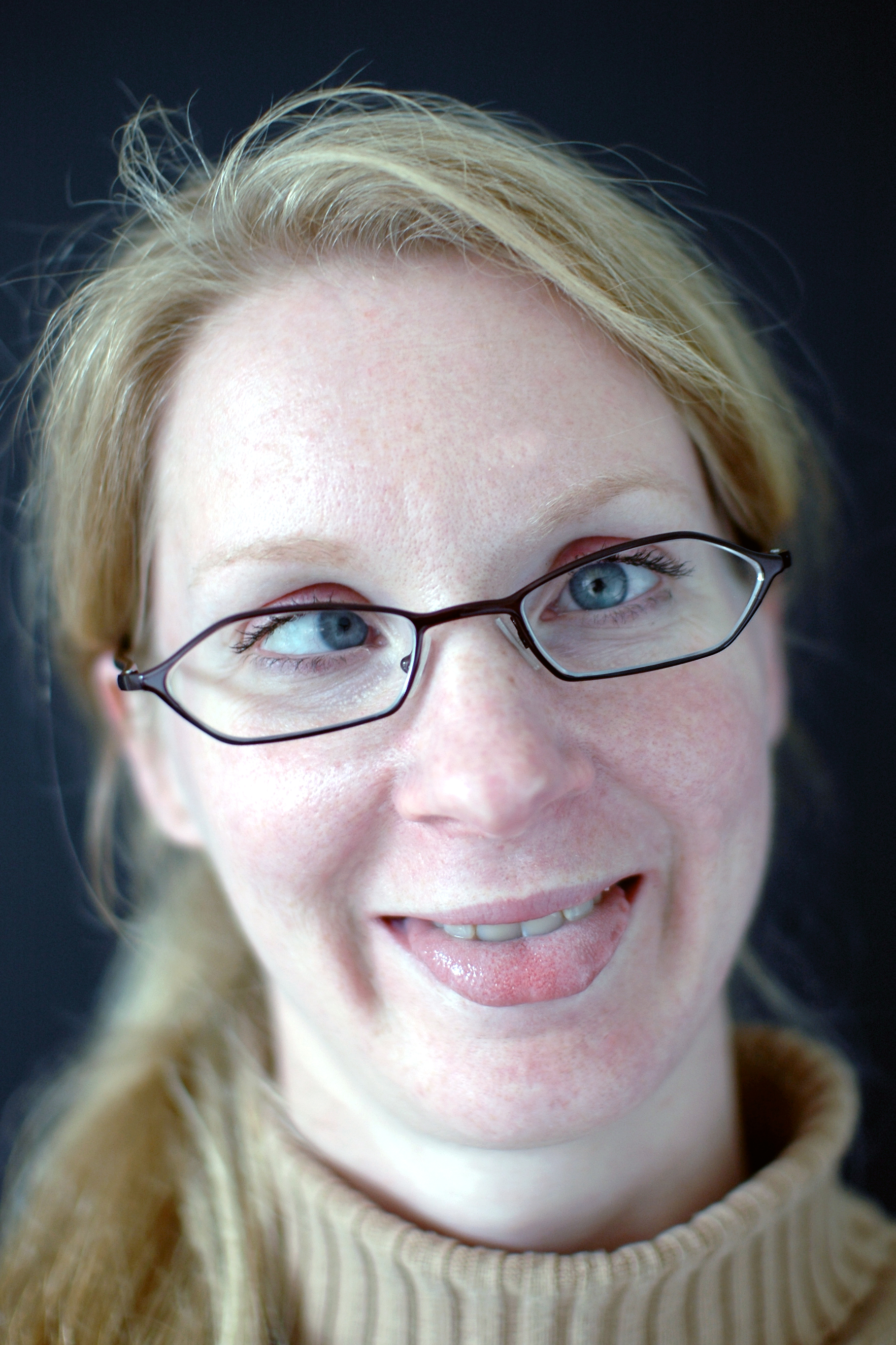 A woman with glasses makes a playful face, crossing her eyes and sticking out her tongue slightly.