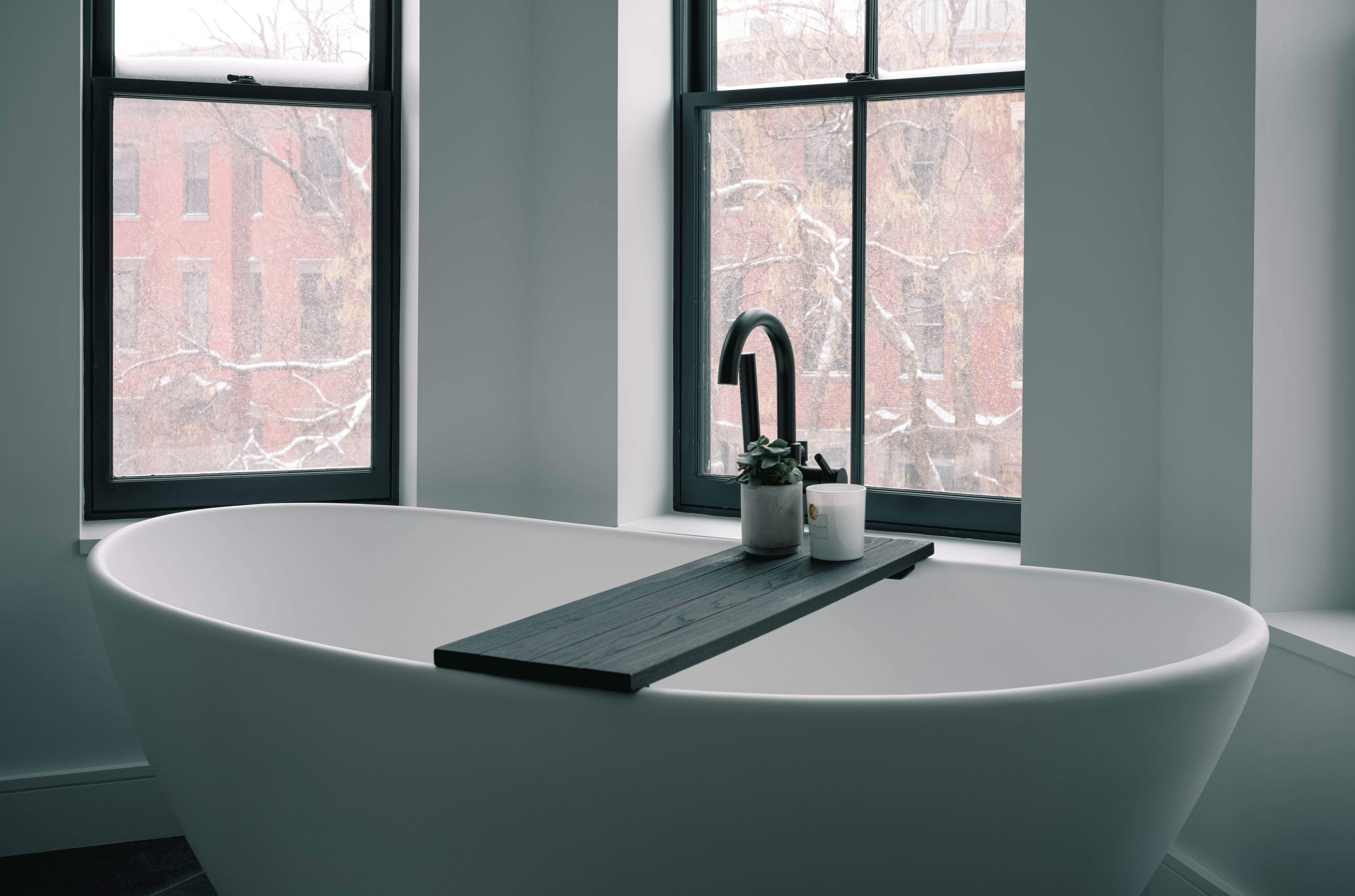 A white bathtub with a black ledge and a window above it.