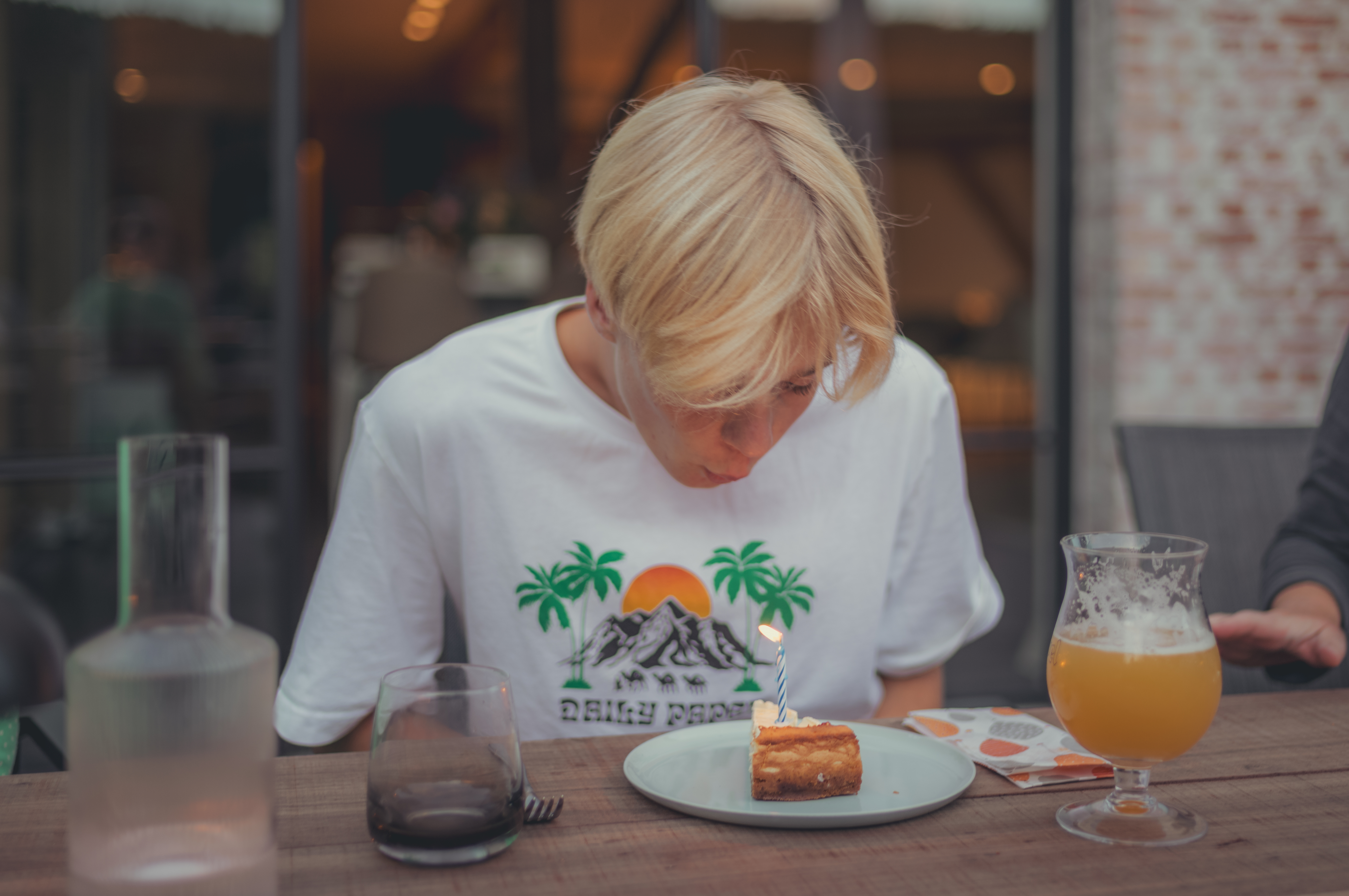 A person leans over to blow out a candle on top of a slice of cheesecake.