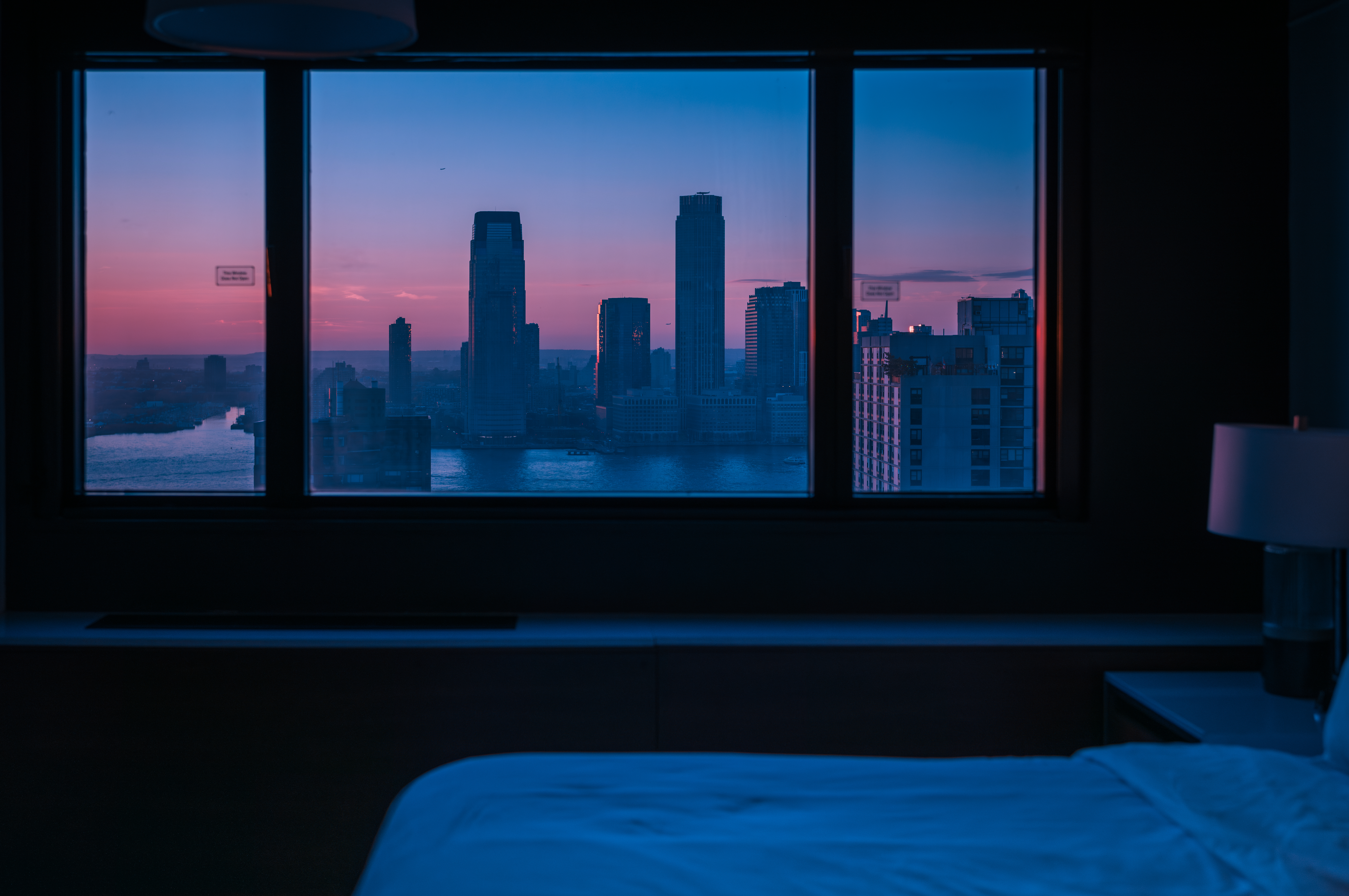 New York City&#039;s skyline seen through a window from a dimly lit hotel room.
