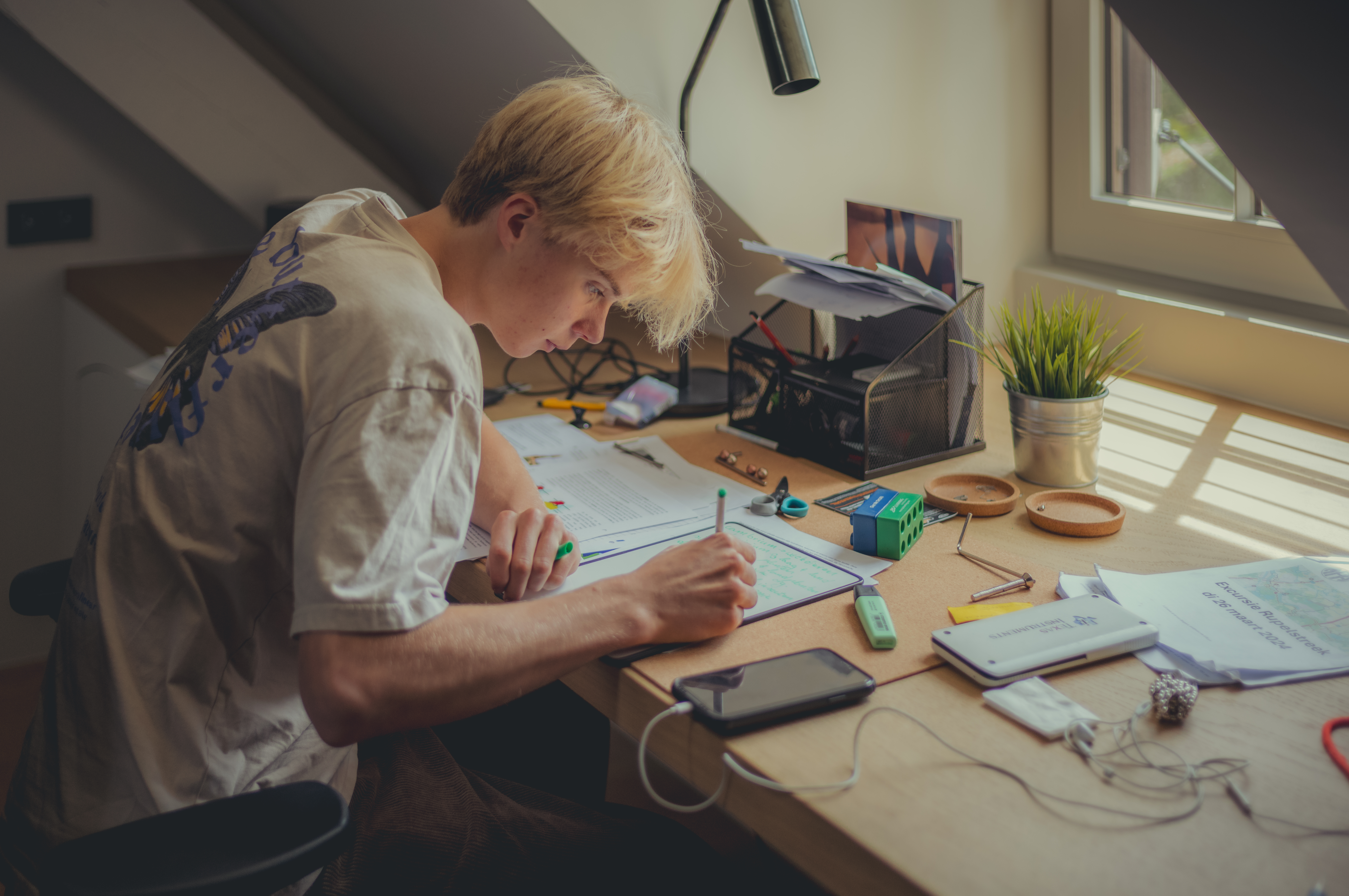 A young man sitting at a desk, writing on a small whiteboard, surrounded by study materials.