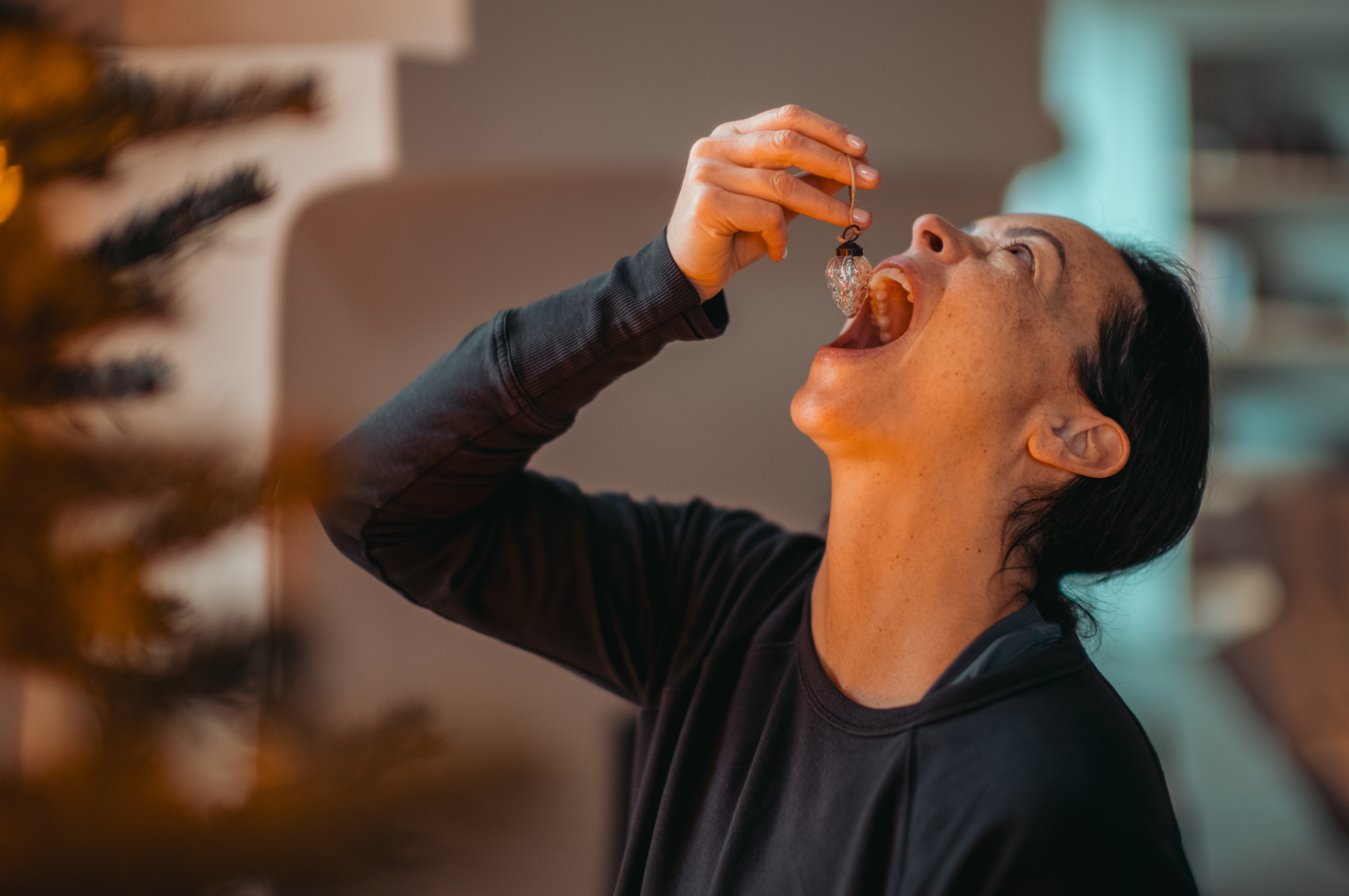A woman playfully pretending to eat a Christmas tree ornament.