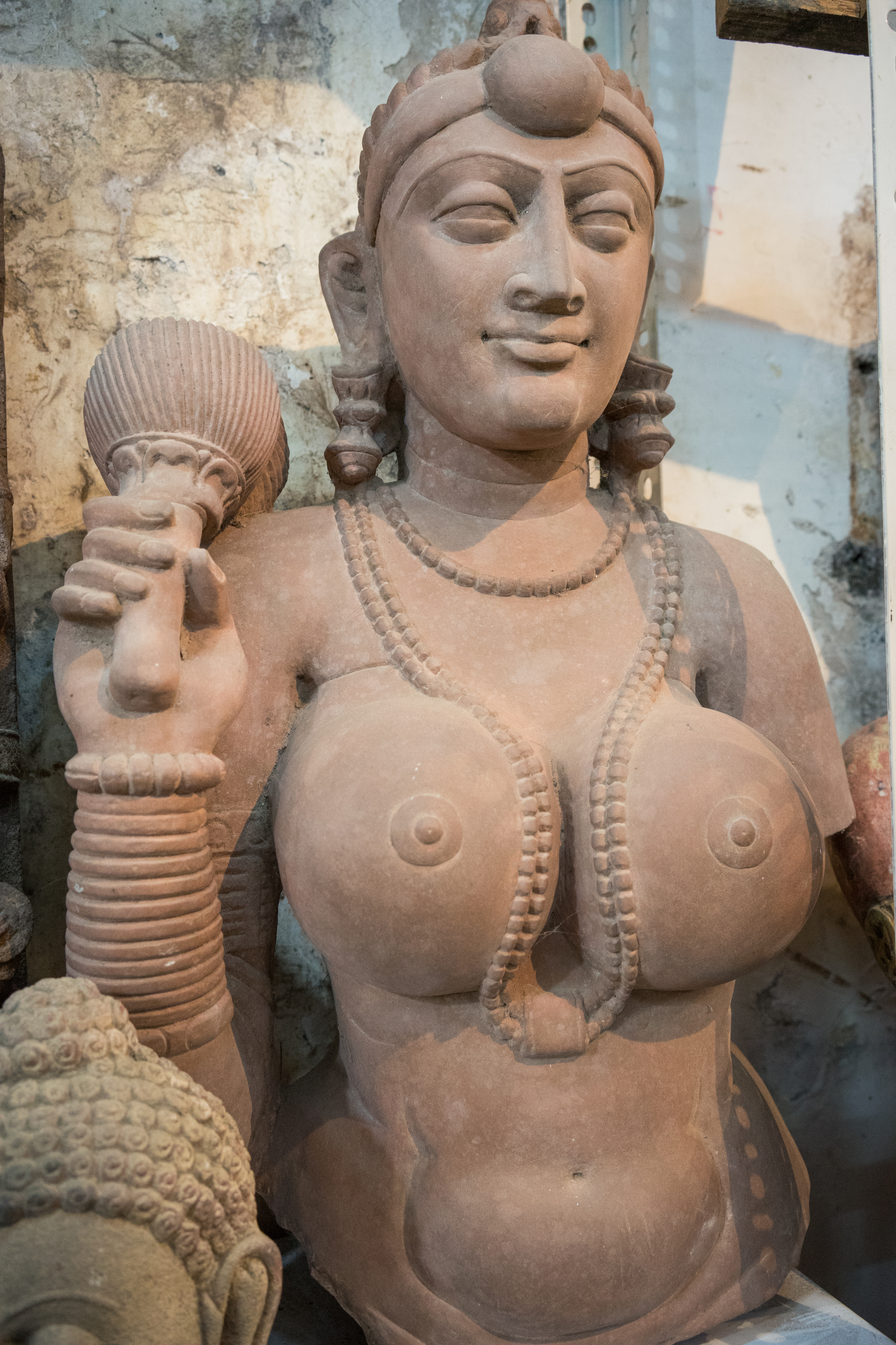 A stone statue of a woman wearing jewelry, holding an object in one hand, with a calm facial expression.