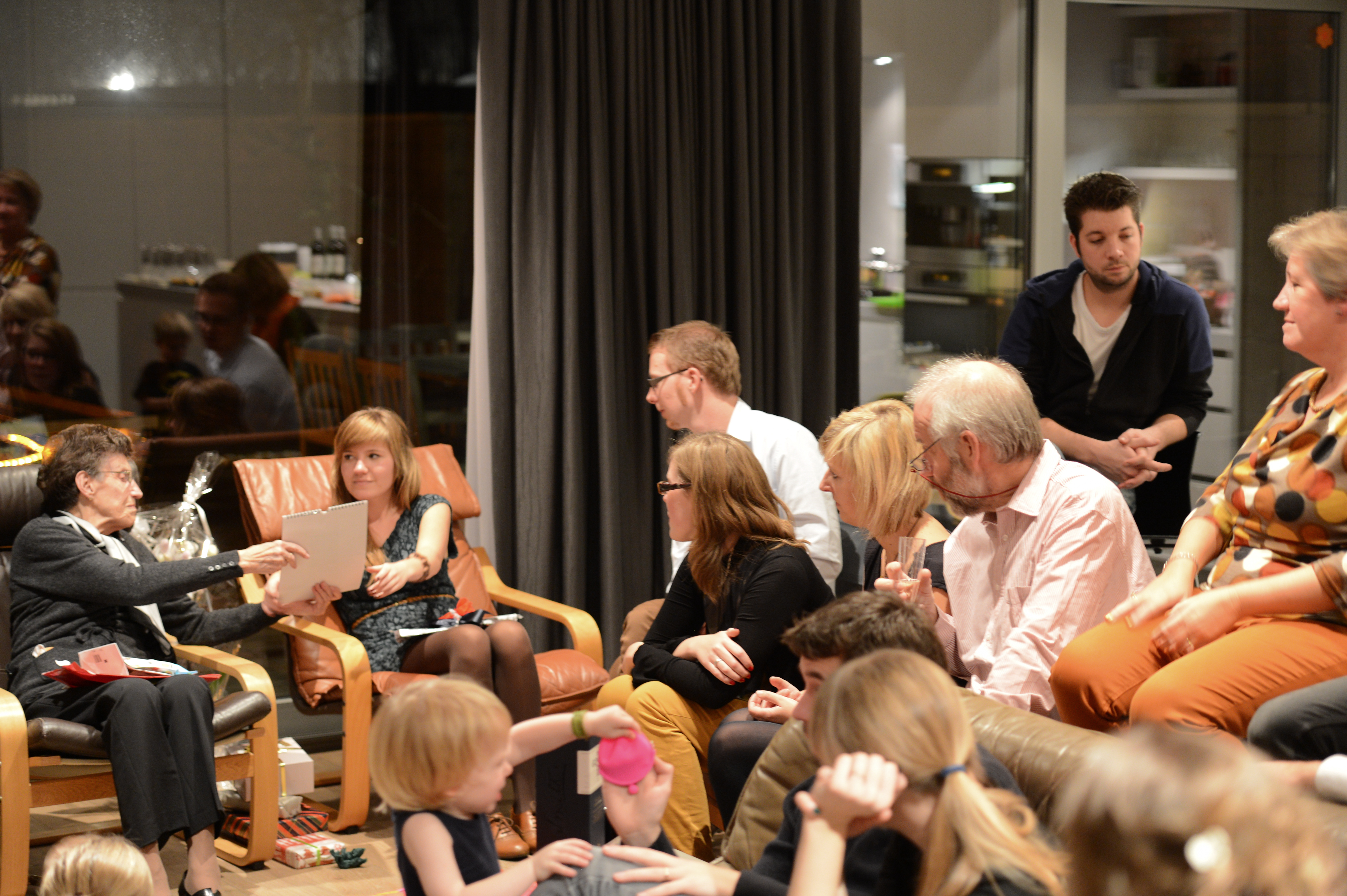 A group of people gathers indoors, talking and exchanging gifts during a New Year's party.