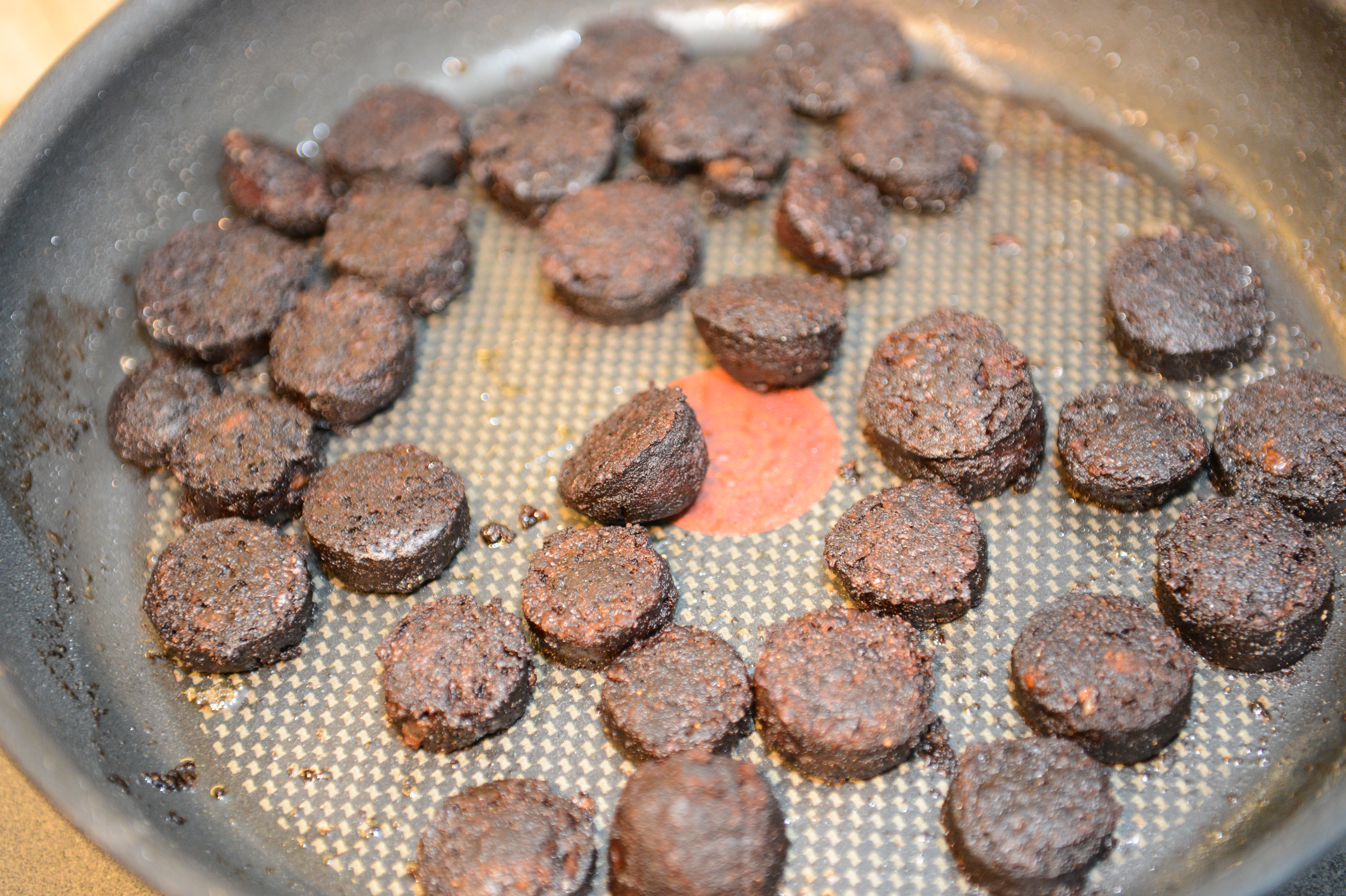Burnt sausage slices in a frying pan with oil residue.