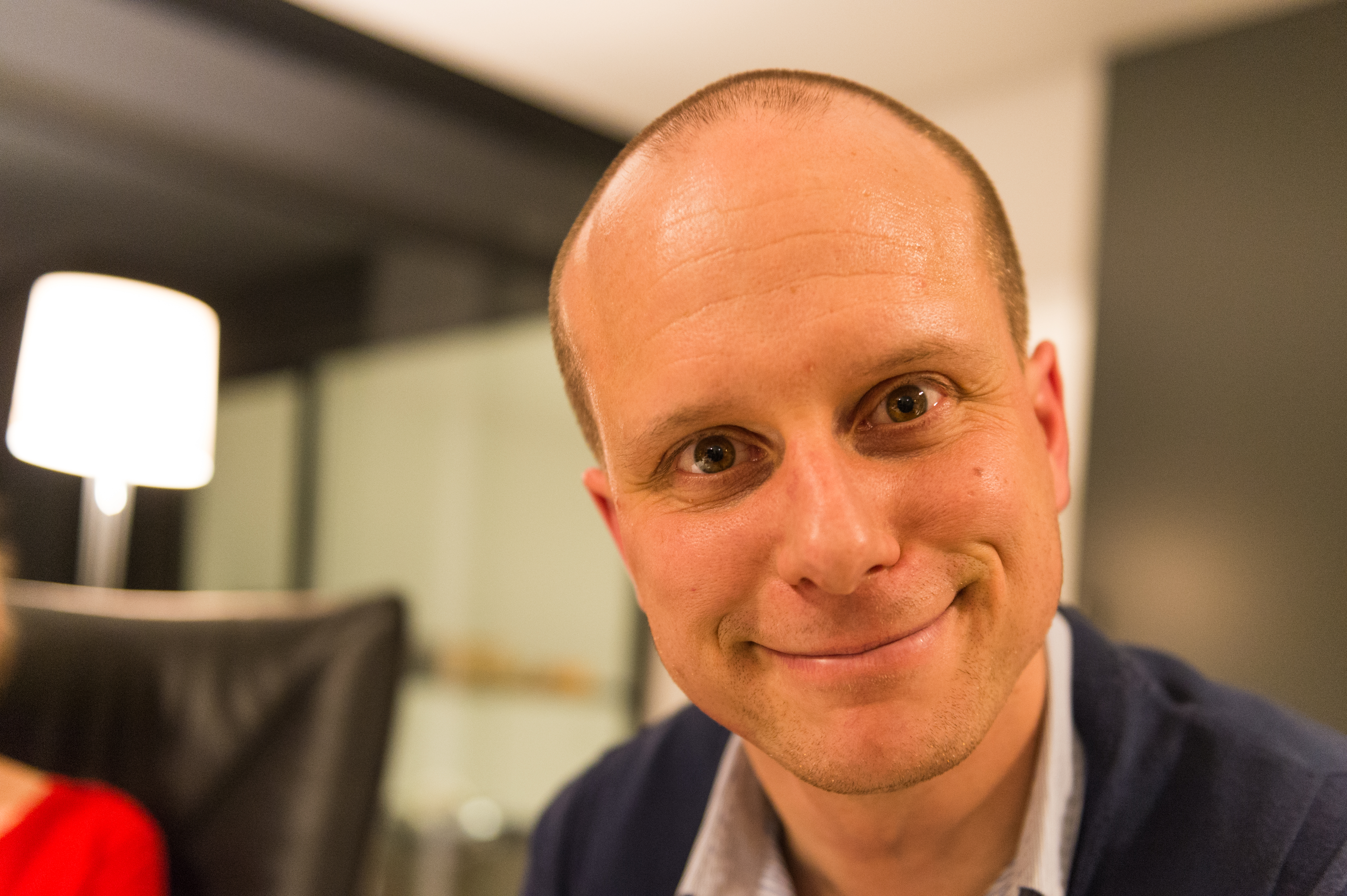 A man in a dark sweater smiles closely at the camera during a New Year's Eve party.
