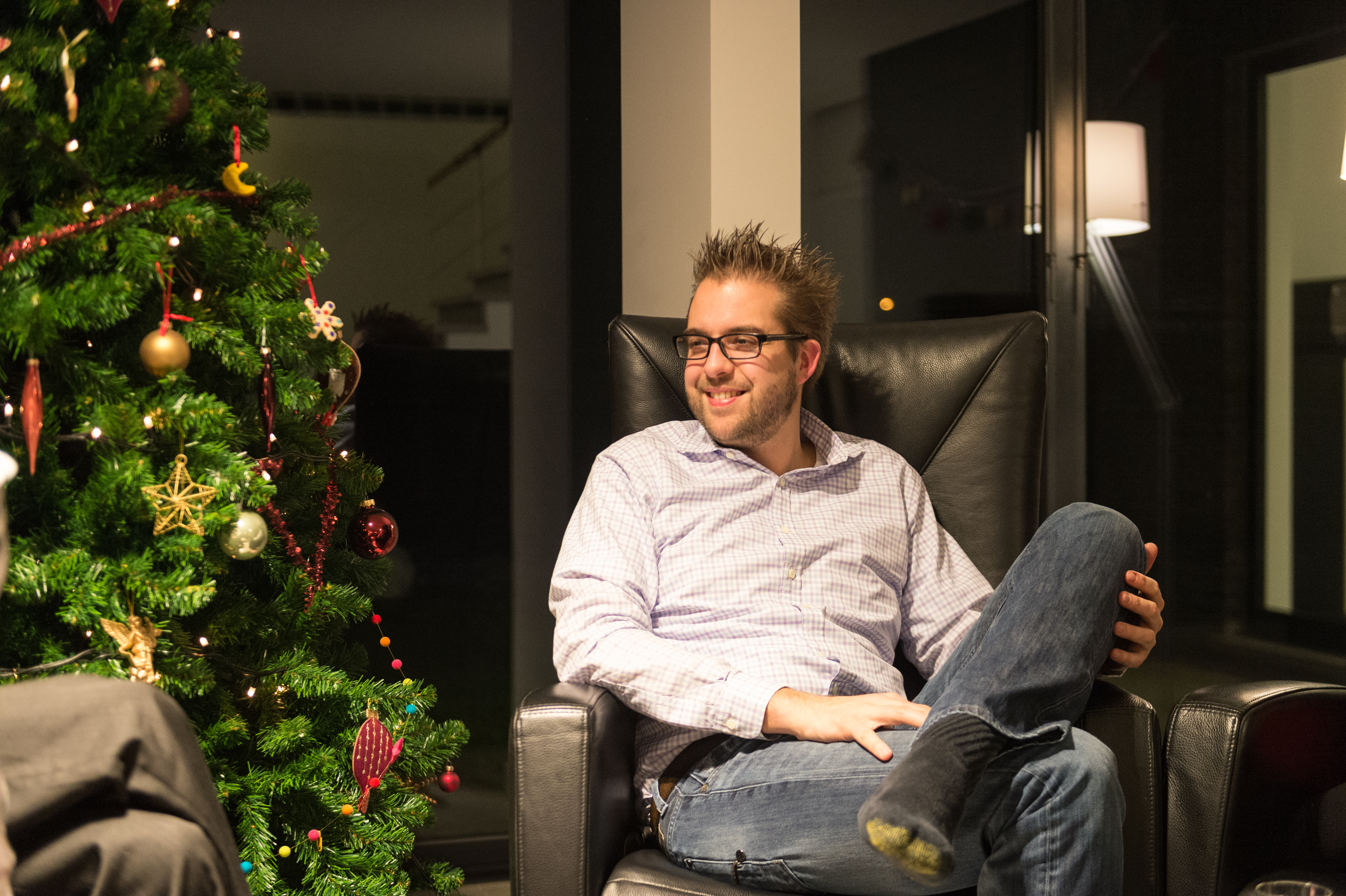 A man wearing glasses sits in a chair, smiling and talking.