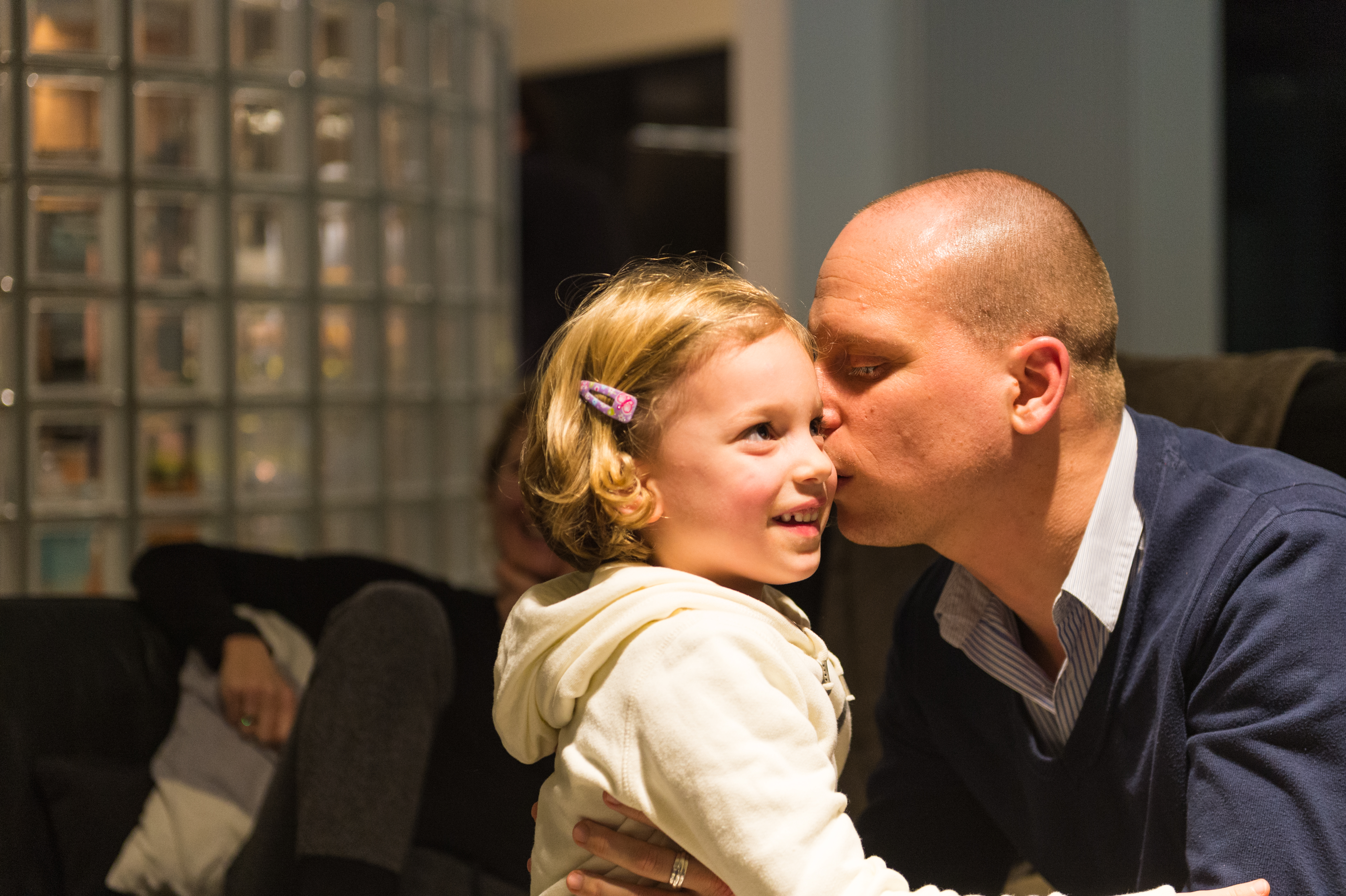 A man in a blue sweater kisses a smiling young girl on the cheek at a party.
