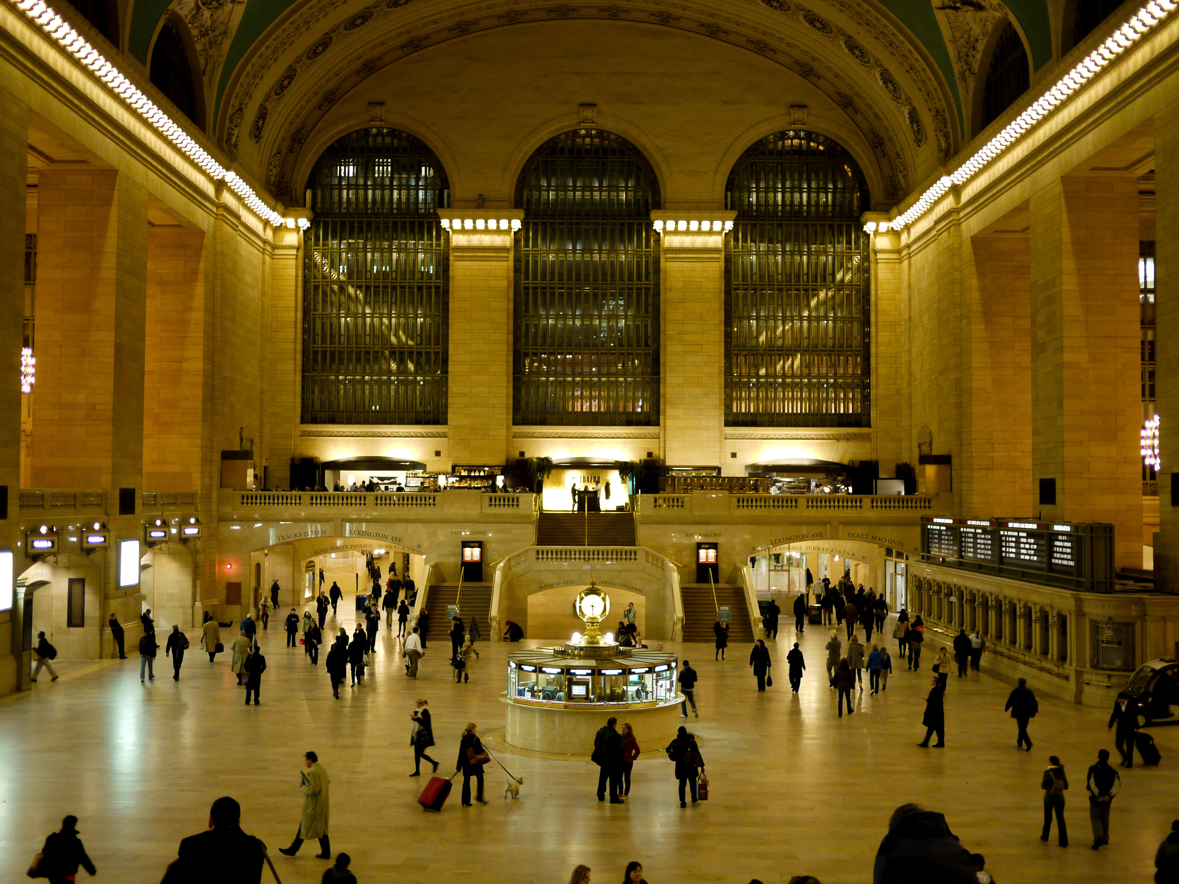 Grand Central Terminal&#039;s main hall with people walking, a central information booth, and large windows in the background.