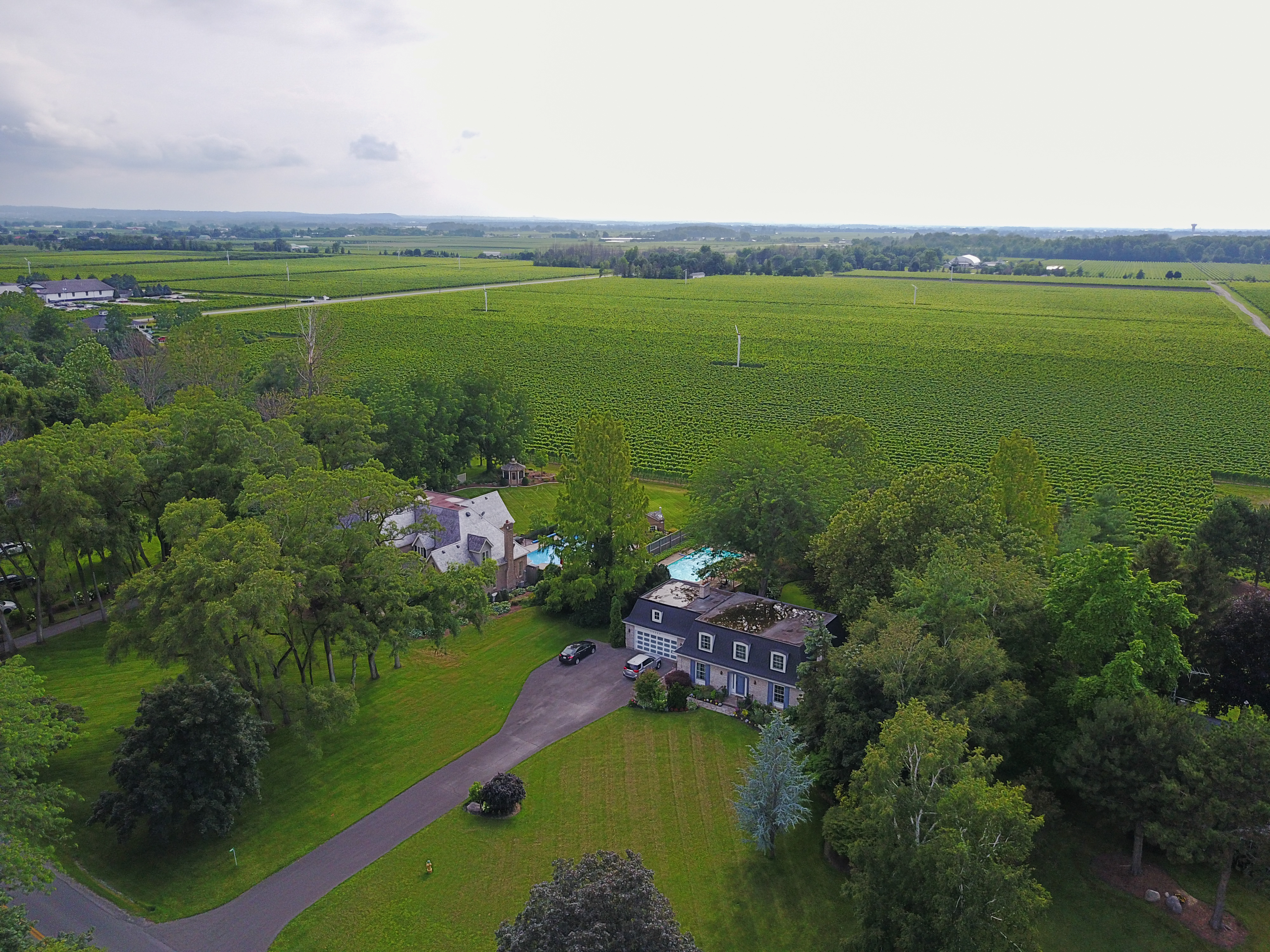 A large house with a swimming pool is surrounded by trees and farmland, viewed from above.