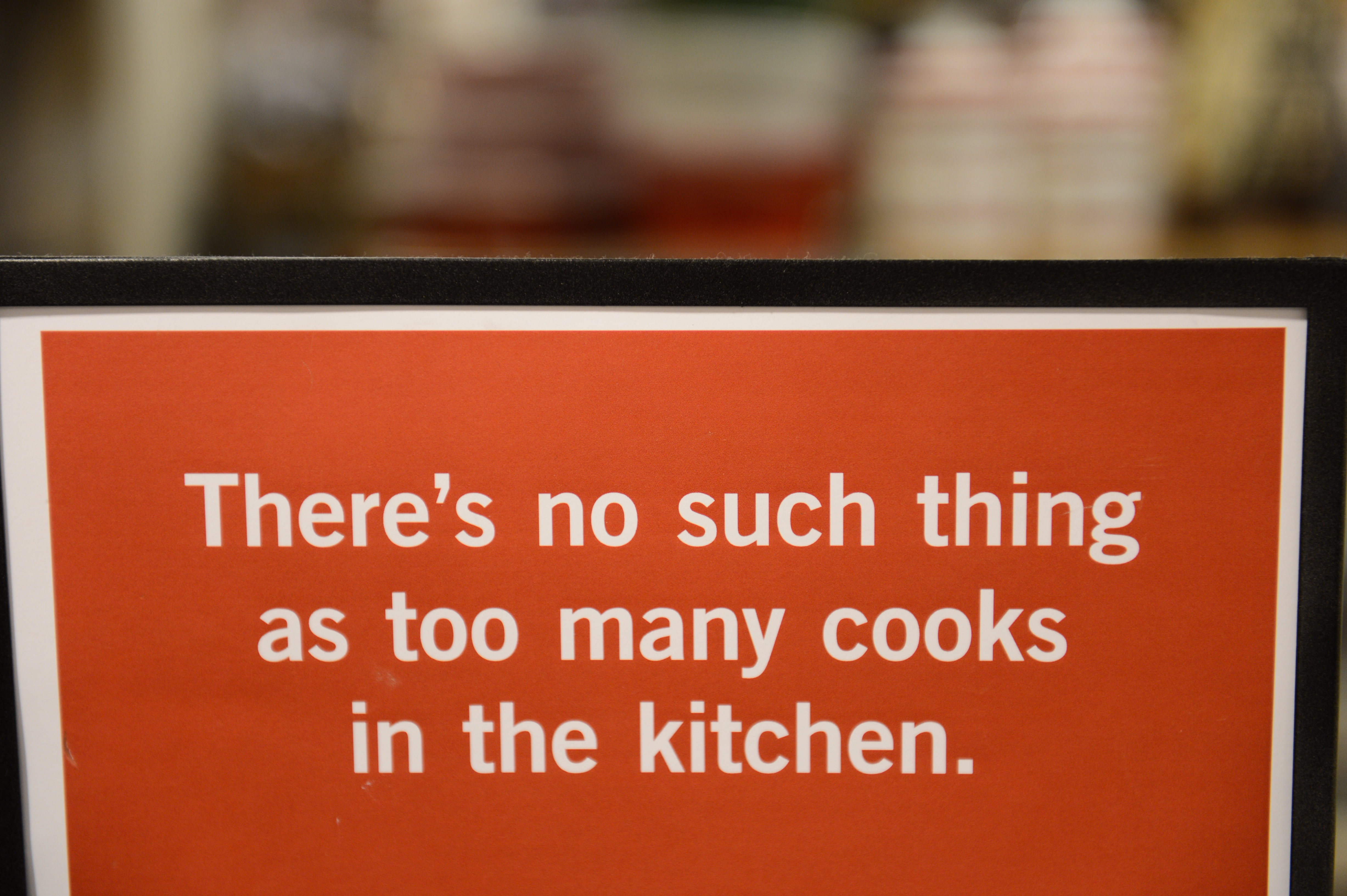 A sign with white text on a red background reads, "There's no such thing as too many cooks in the kitchen.