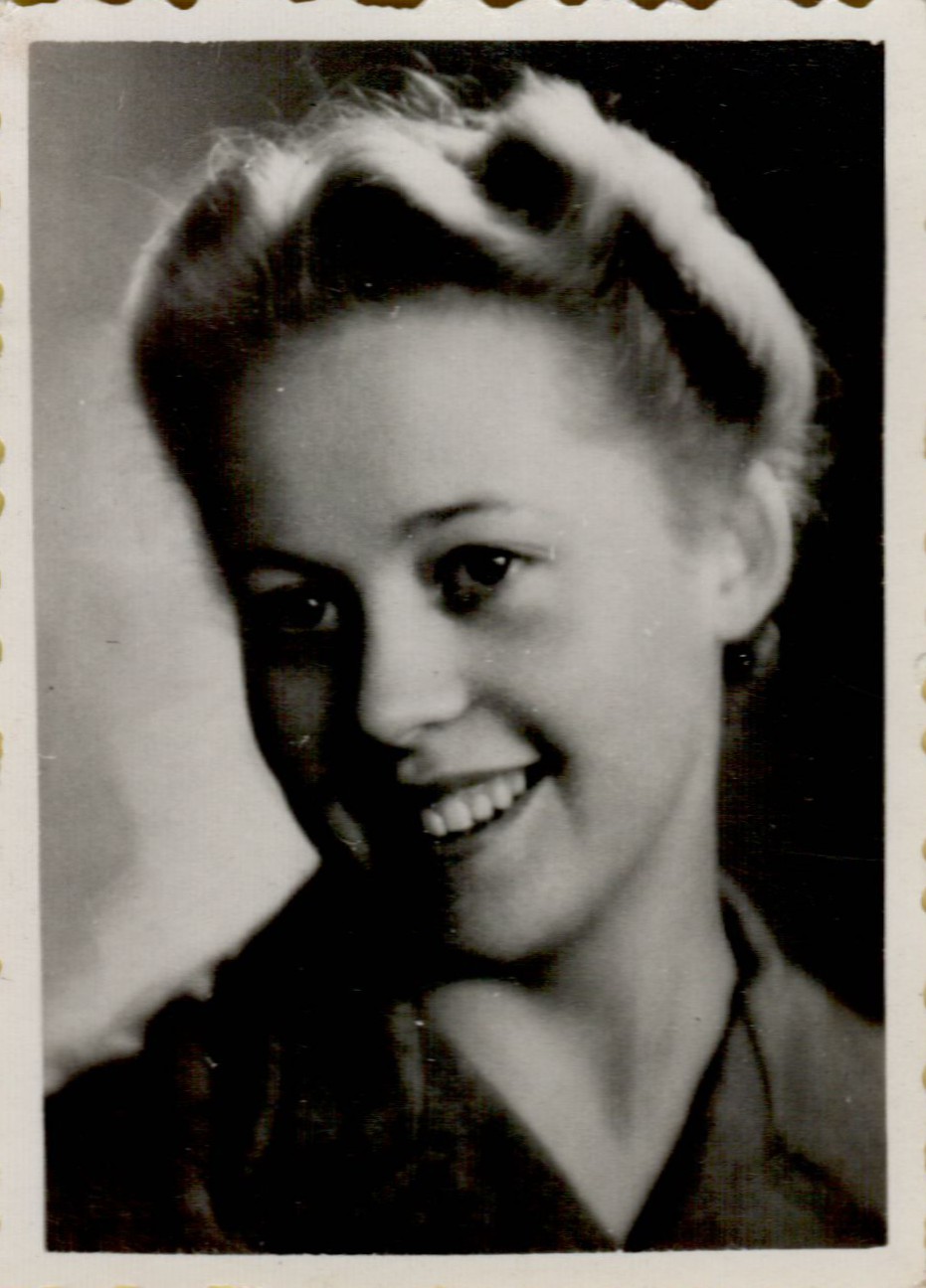 A black-and-white portrait of a smiling woman with styled hair, wearing a collared outfit, looking slightly sideways.