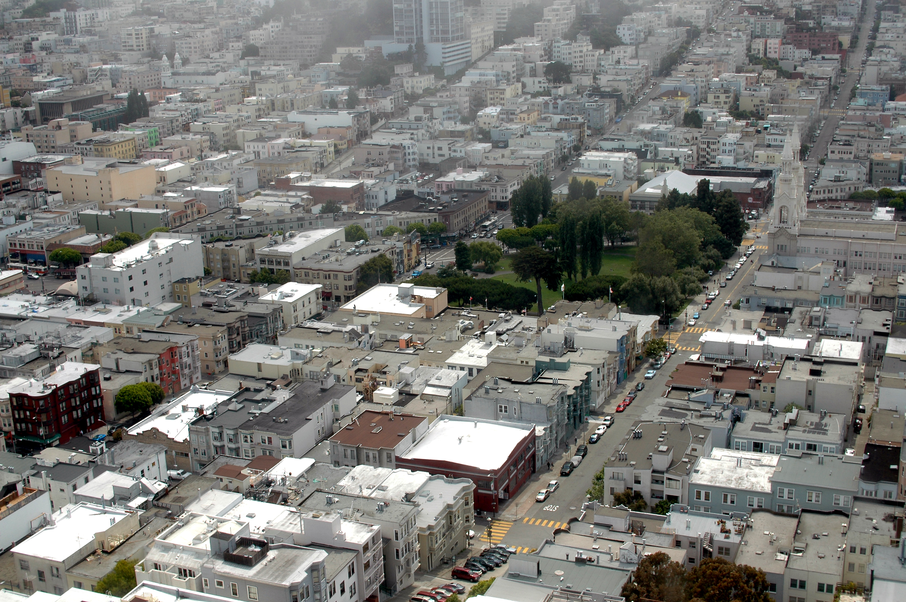 Aerial view of a dense urban neighborhood with tightly packed buildings, streets, and a small park in the center.