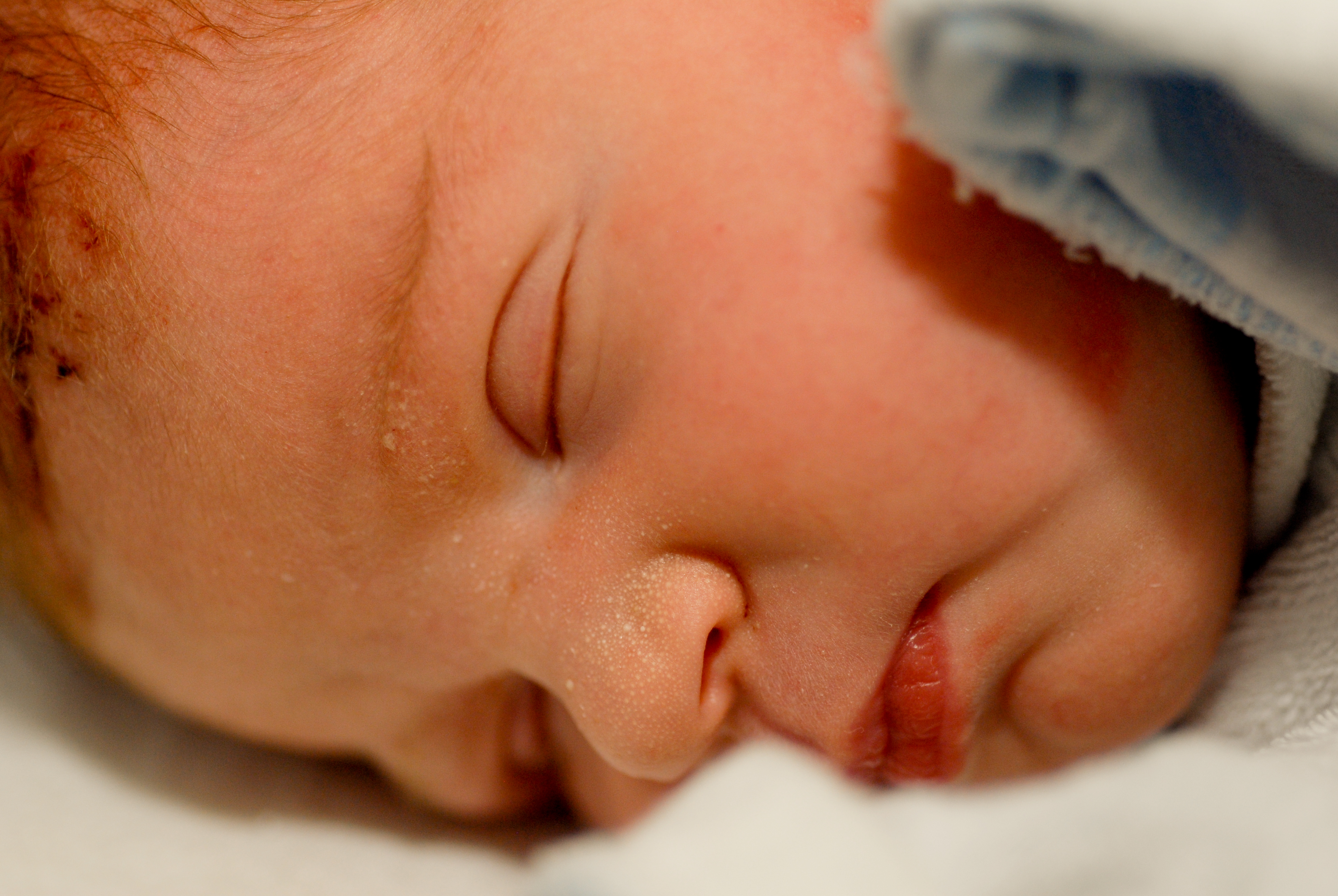 Close-up of a newborn baby sleeping, wrapped in a soft blanket with eyes closed and lips slightly parted.