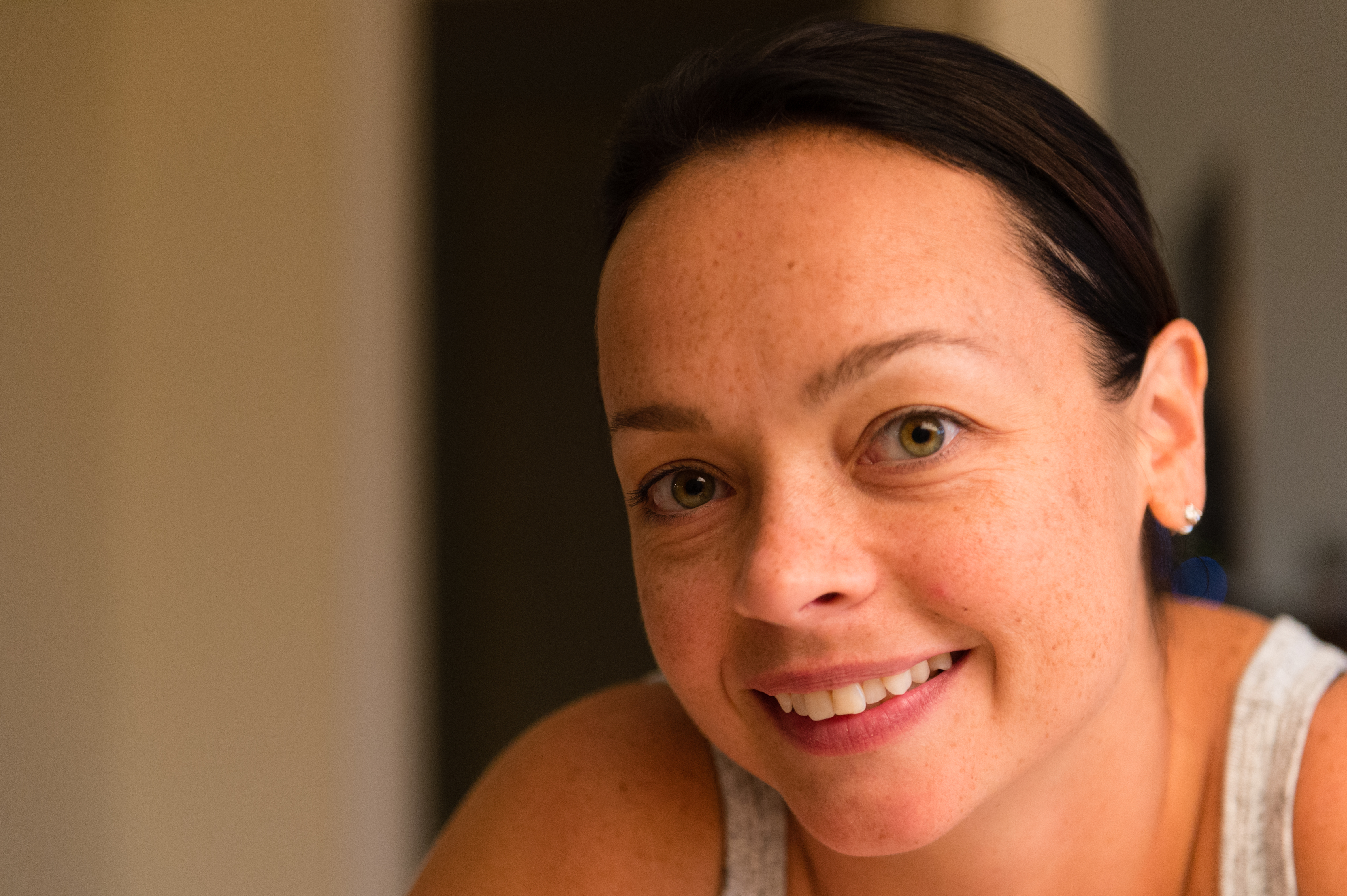 A person with dark hair and a smile looks directly at the camera in a warmly lit indoor setting.