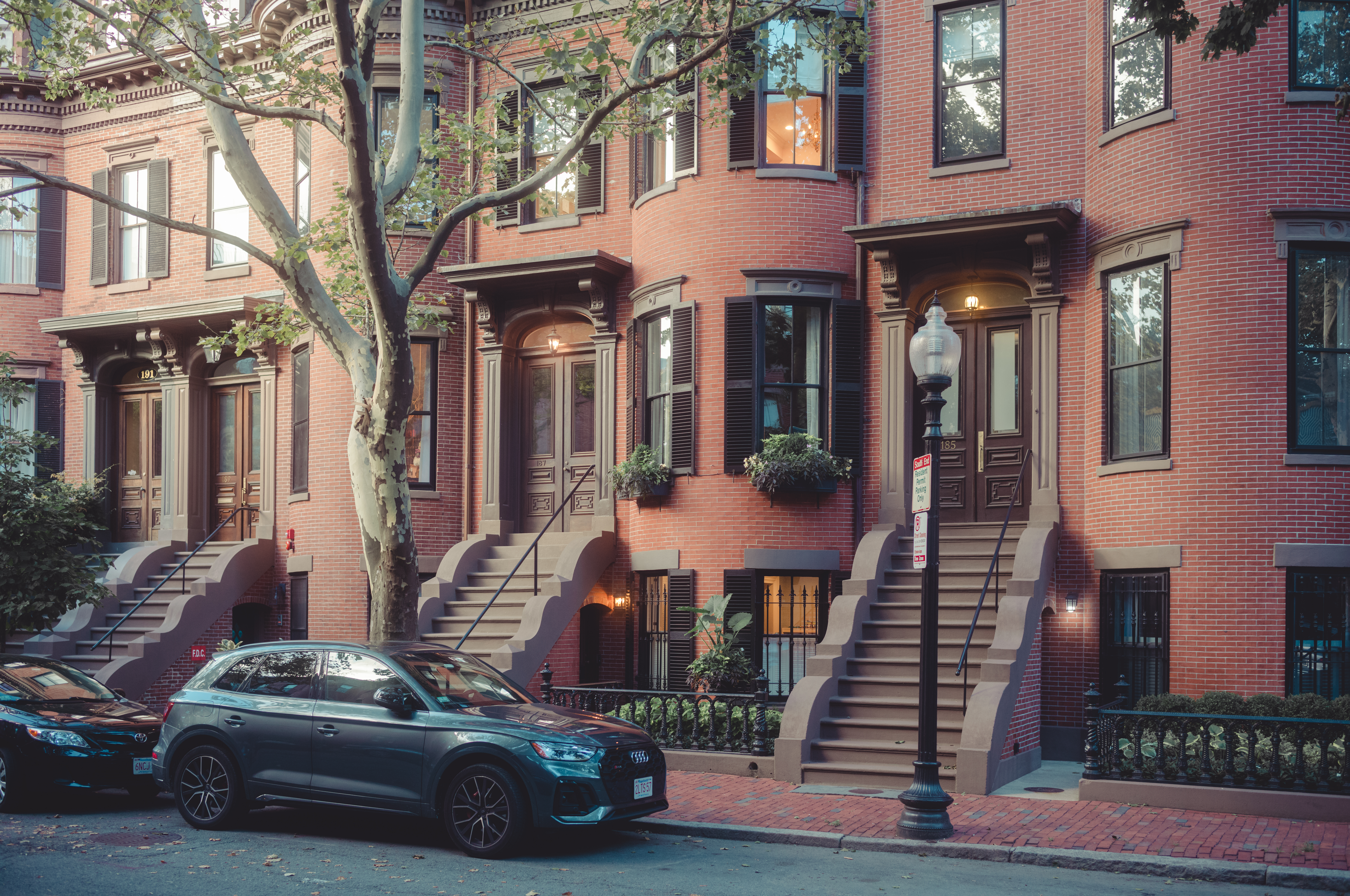 Red brick townhouses with brownstone steps in Boston&#039;s South End, with parked cars and a streetlamp in front.