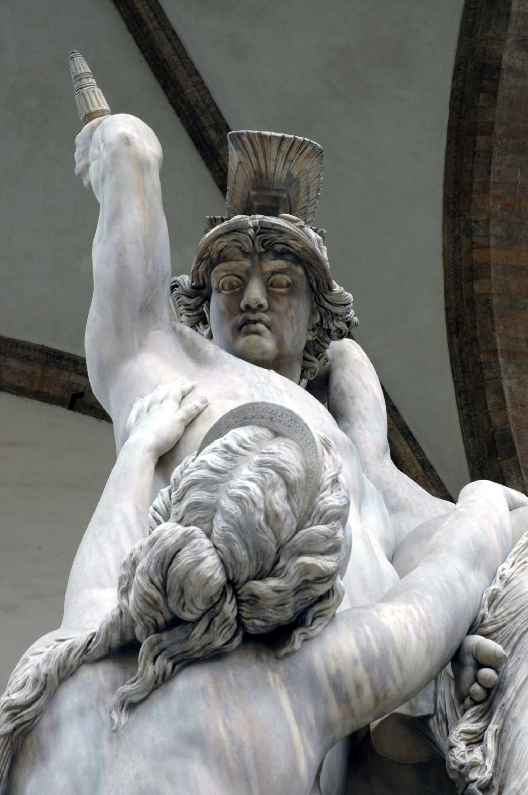 Marble statue of a warrior in a helmet holding a struggling figure, with intense expressions and dynamic movement.