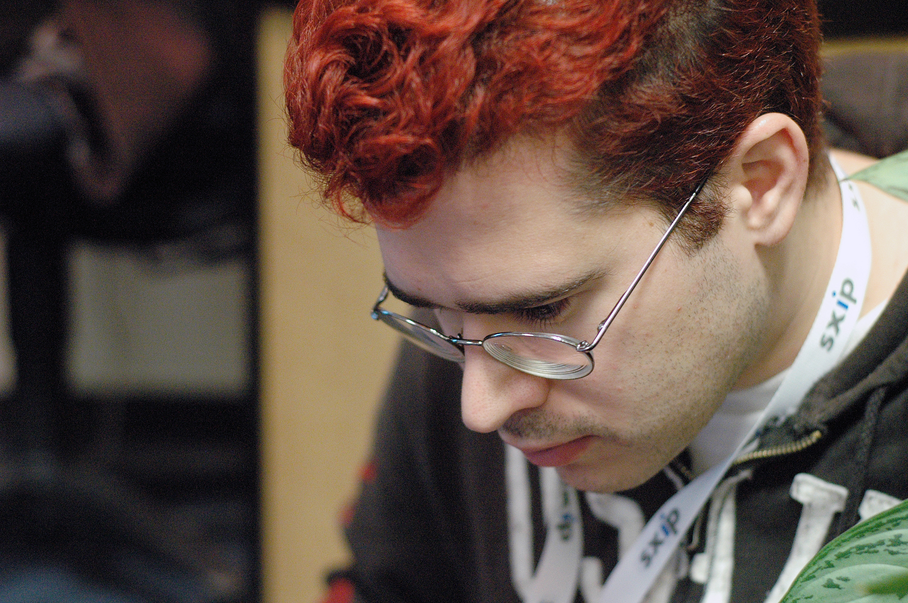 A person with red hair and glasses looks down, wearing a lanyard with &quot;sxip&quot; text.