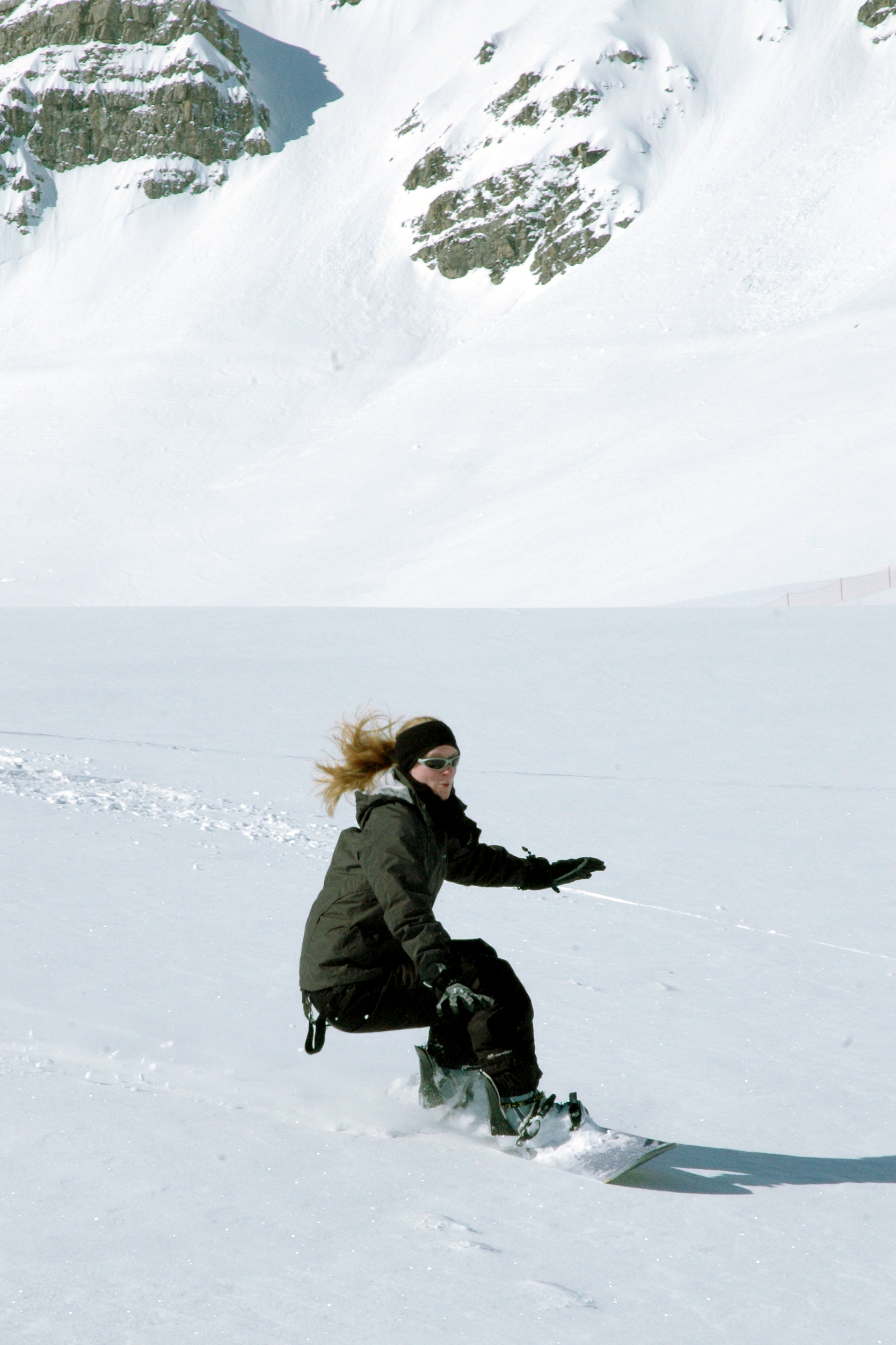 A person in a dark winter outfit snowboards down a snowy slope, balancing with arms outstretched.
