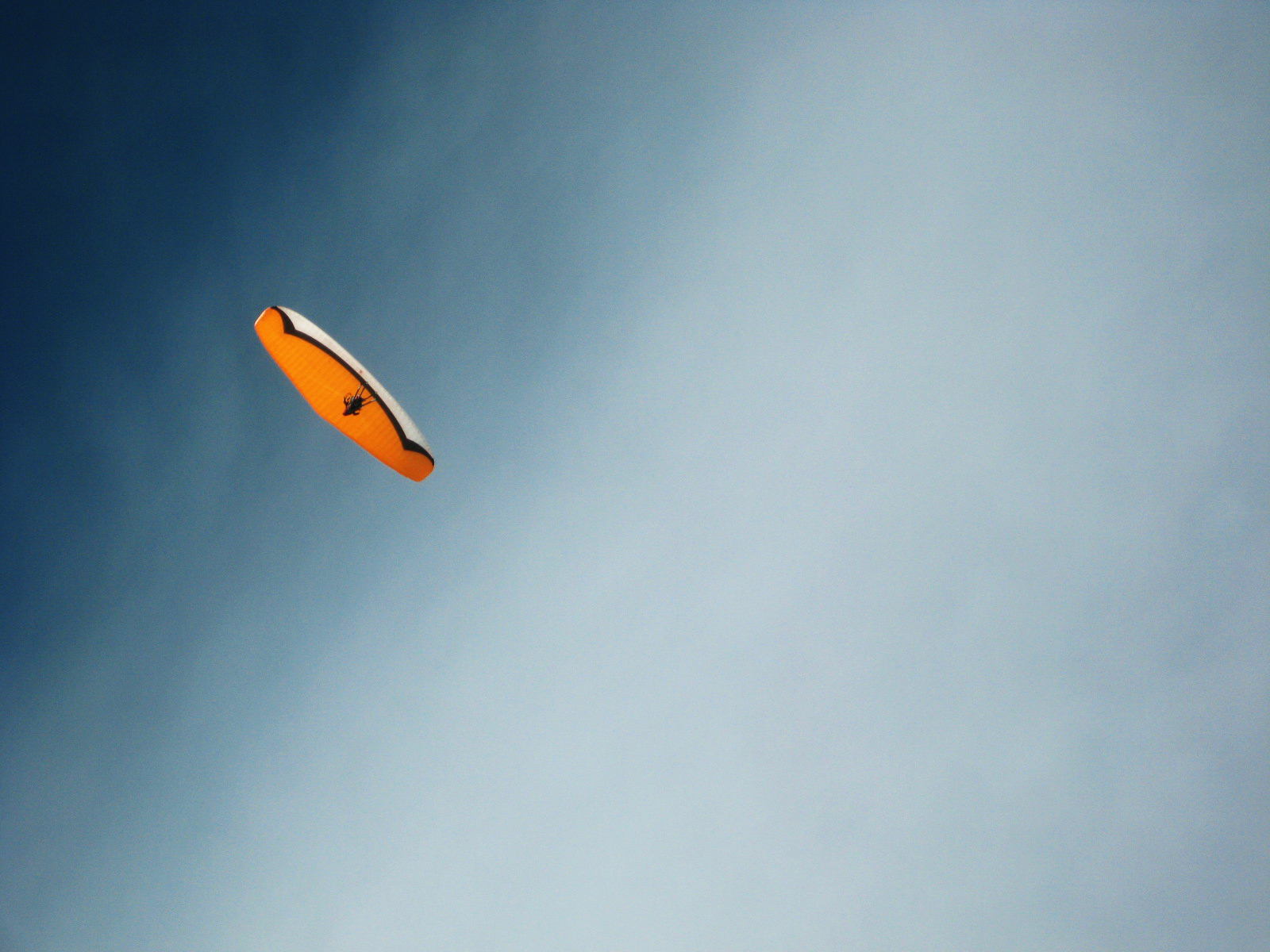 A person paraglides through the sky with an orange and white canopy.