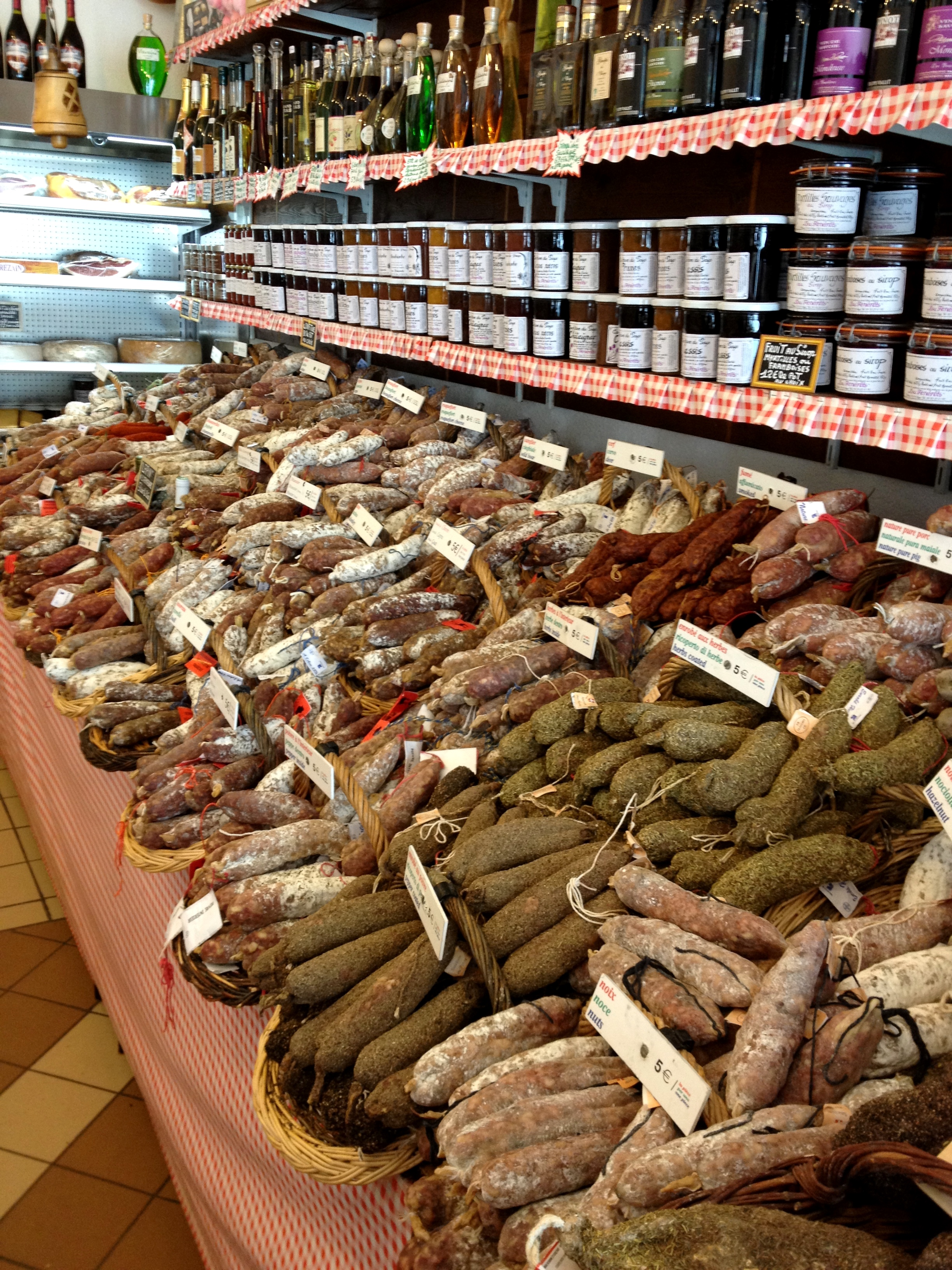A market display with various cured sausages in baskets, labeled with prices.