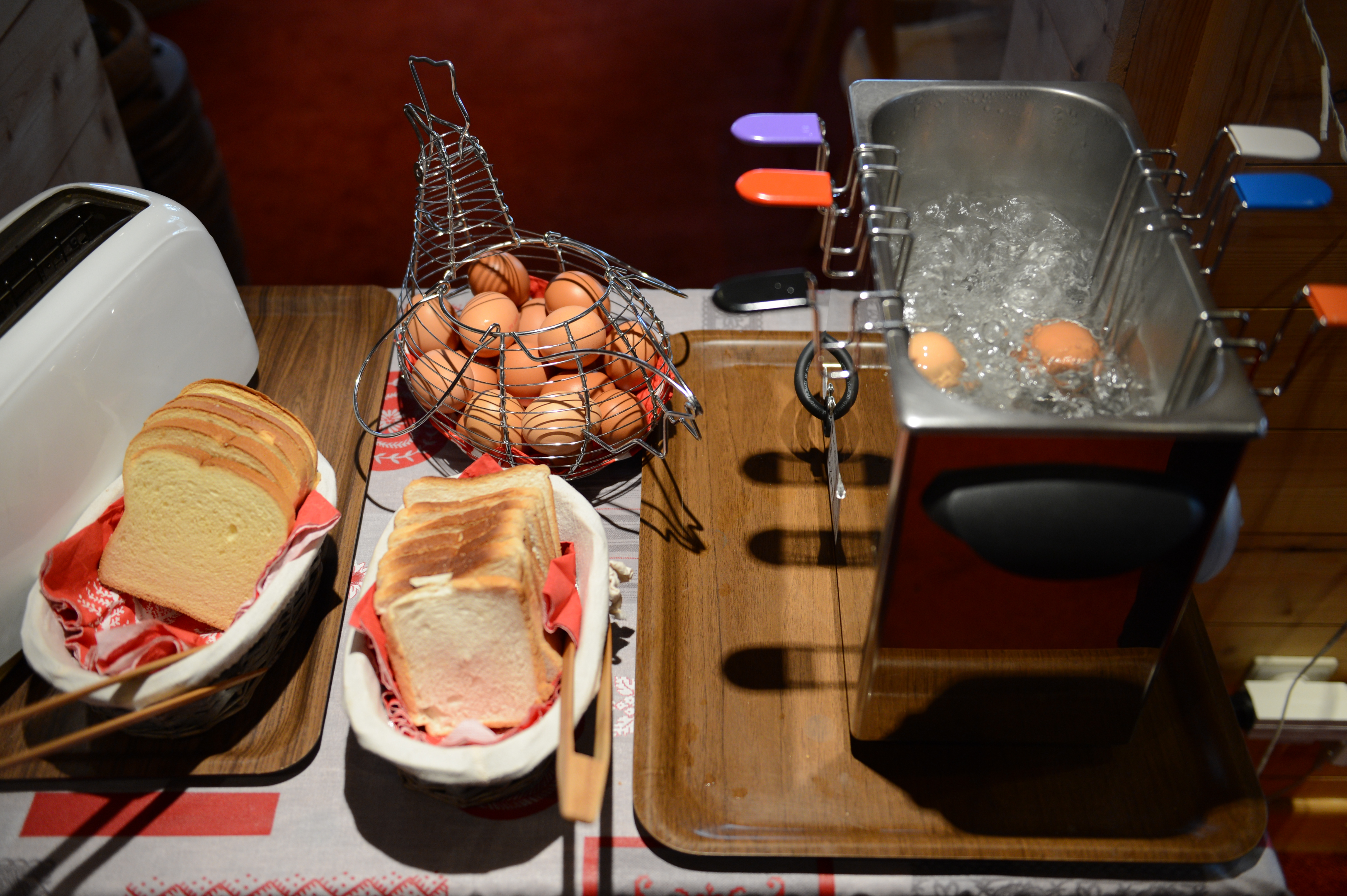 Slices of bread, a toaster, and a basket of eggs next to a boiling egg cooker.
