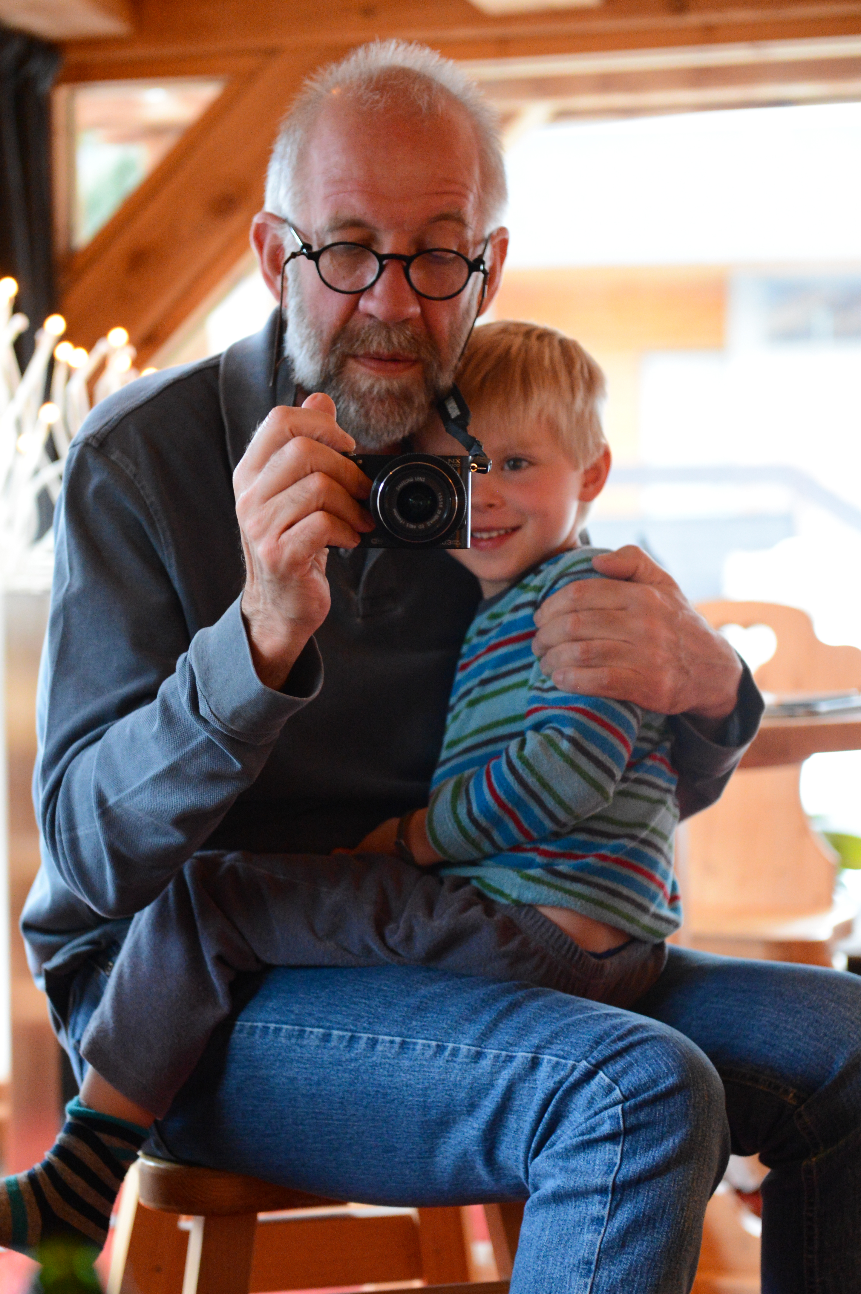 An older man with glasses holds a camera while a young child sits on his lap, smiling.