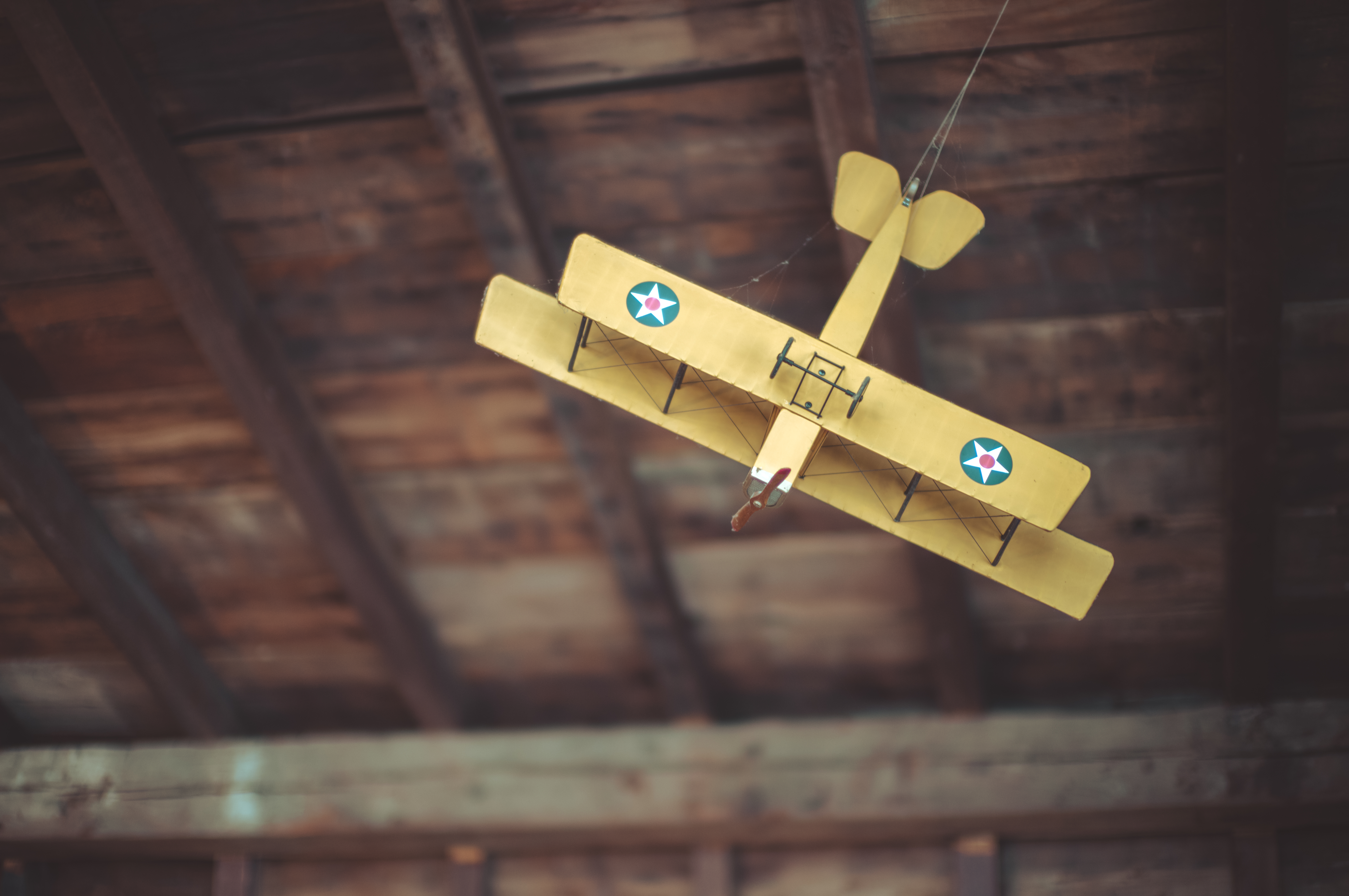 A model plane with a 3-foot or 90-centimeter wingspan hangs from dark wooden beams on the ceiling. It&#039;s an antique biplane with double-stacked wings in bright yellow.