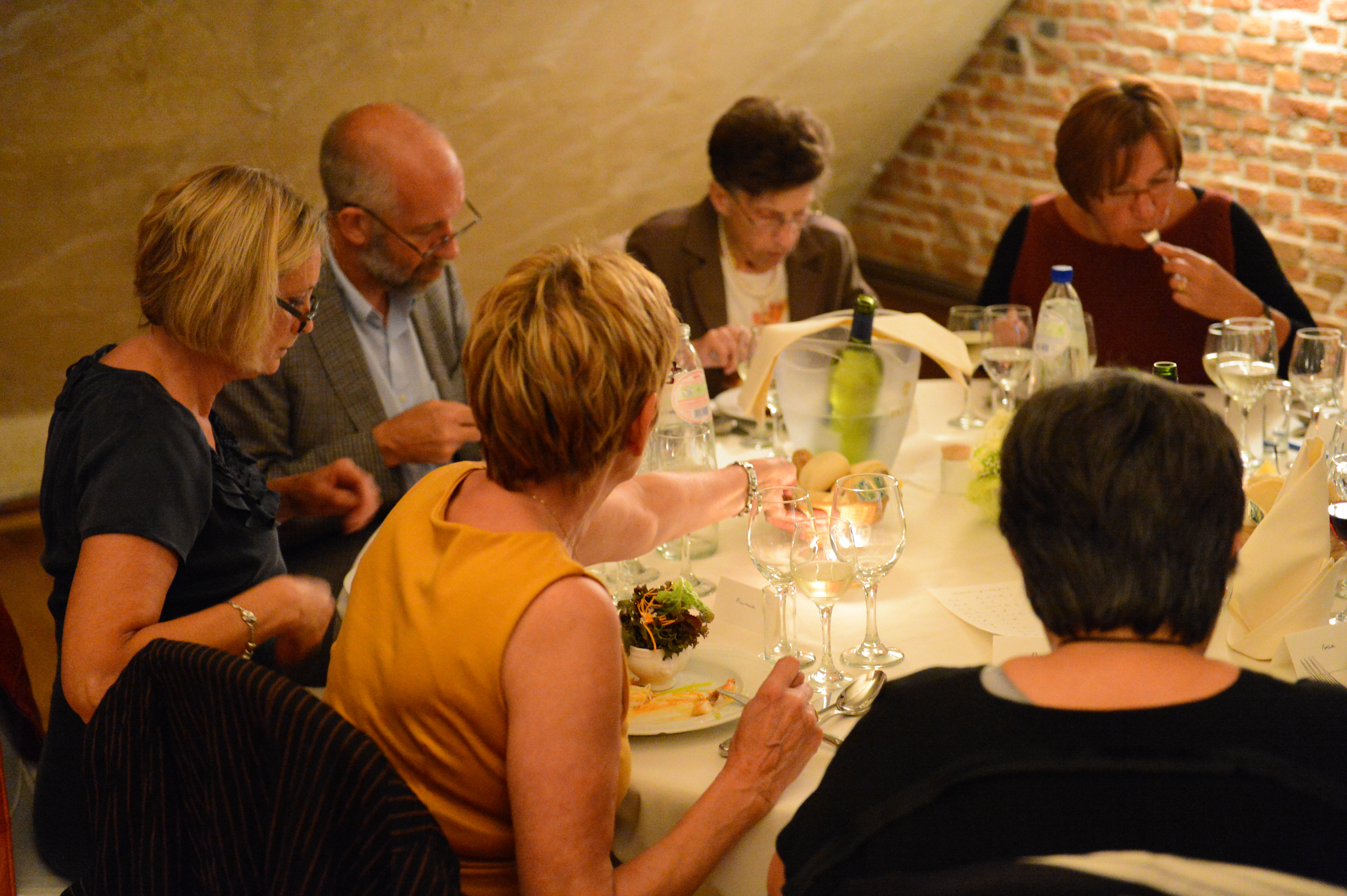 Guests sit around a table at a wedding reception, eating, drinking, and talking.