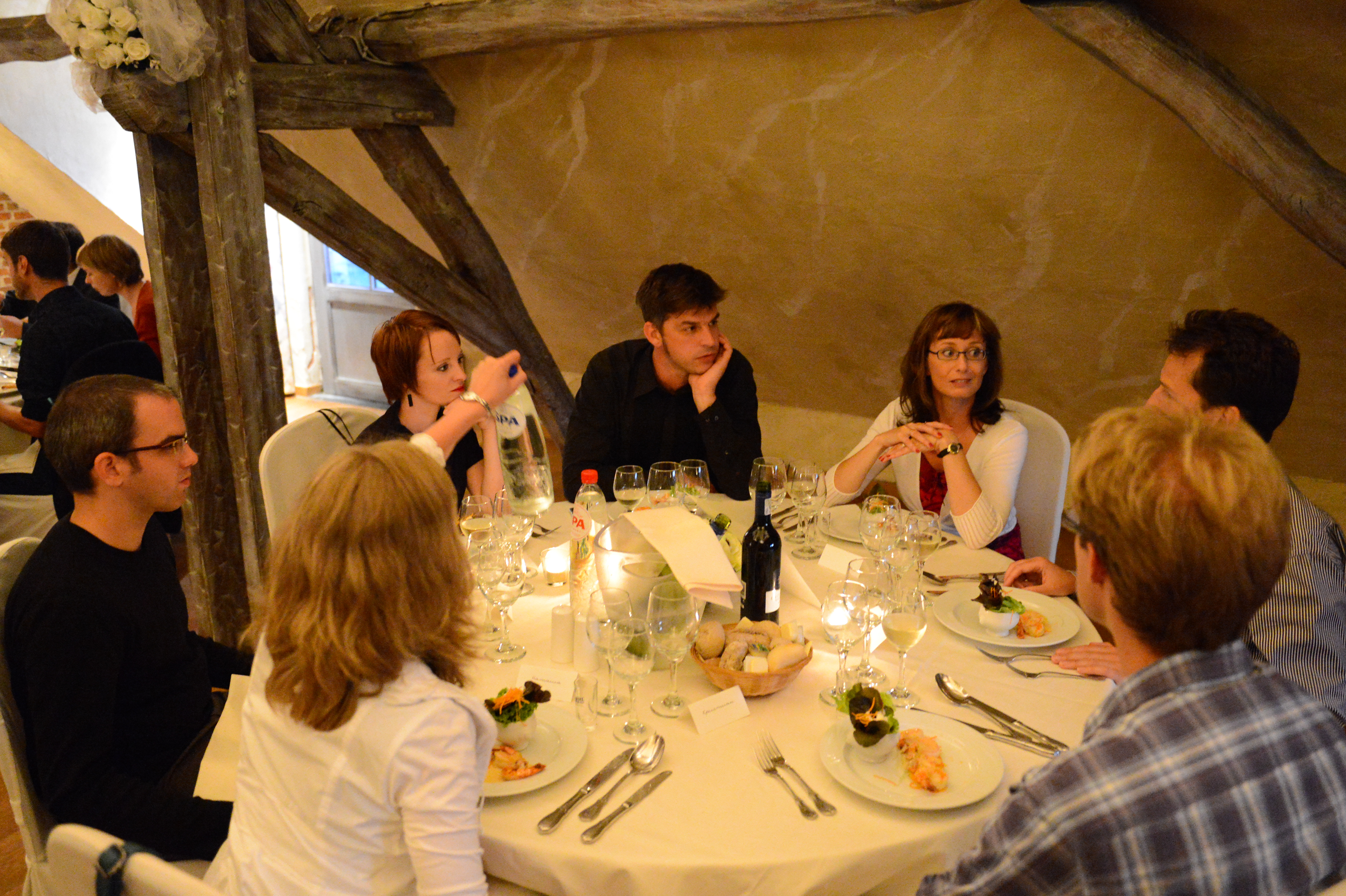 Guests sit around a table at a wedding reception, engaged in conversation while enjoying food and drinks.