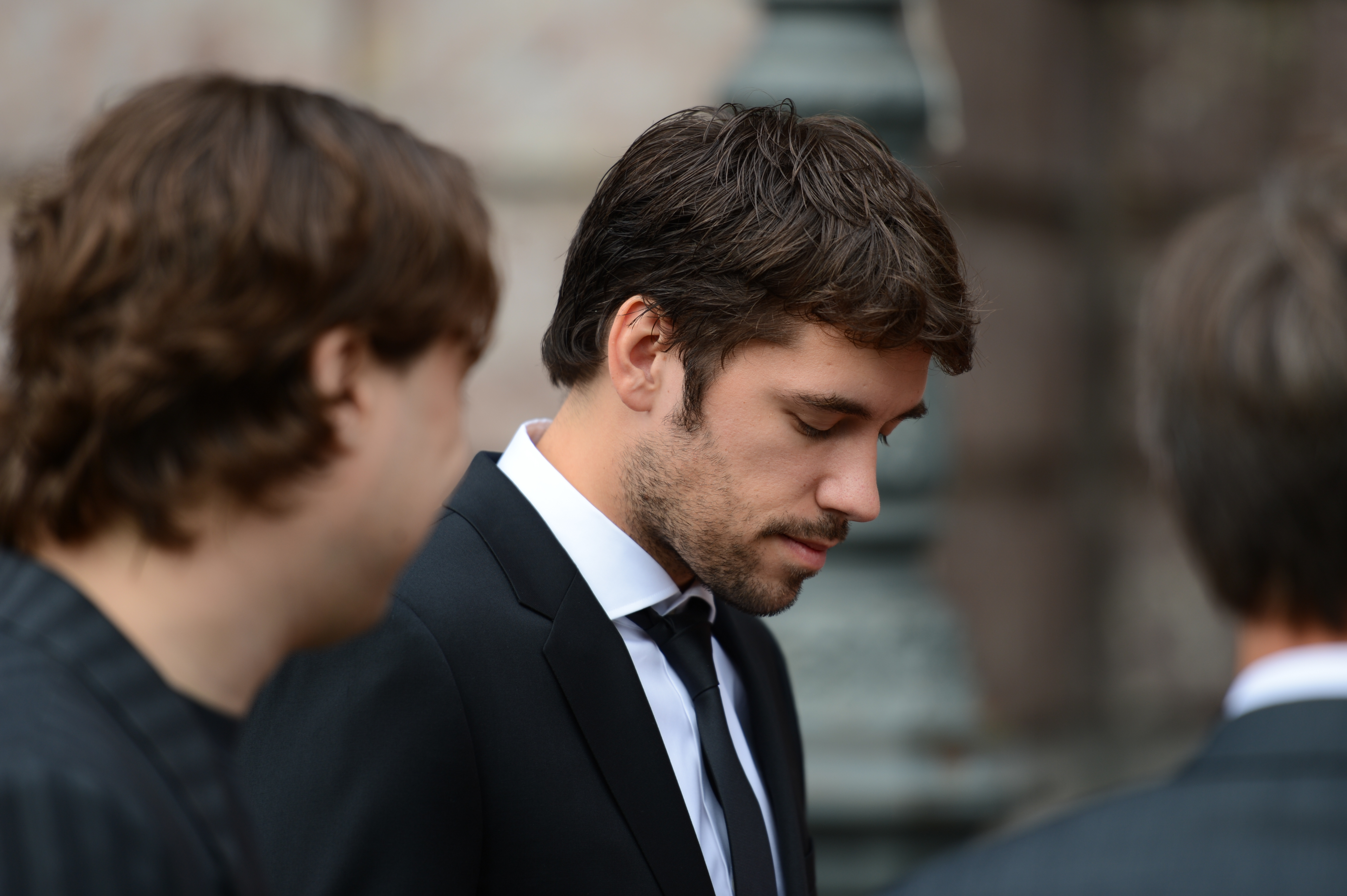 A man in a suit looks down while standing among others at a wedding gathering.