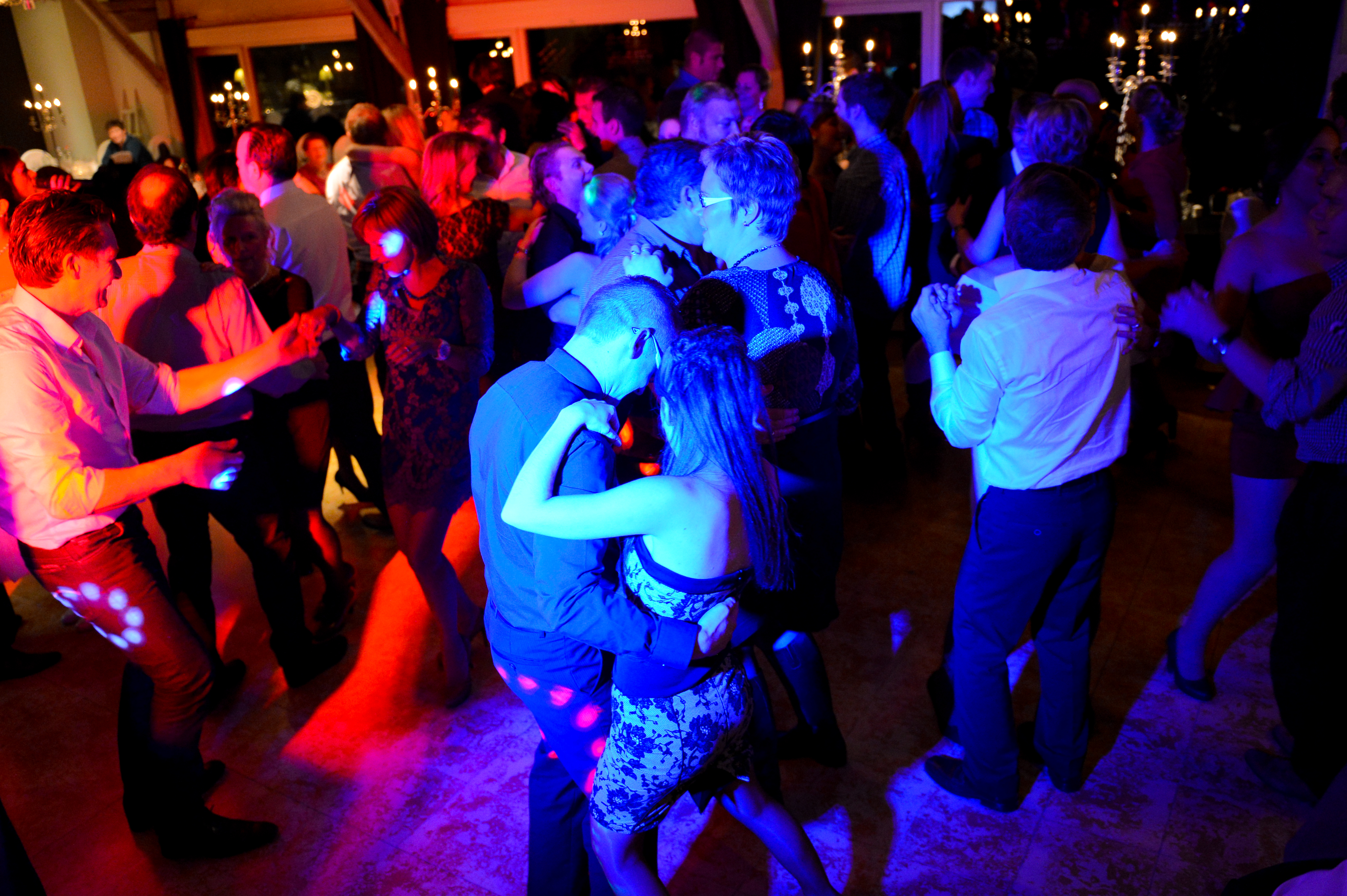 People dancing closely at a wedding reception, surrounded by colorful lights and a lively crowd.