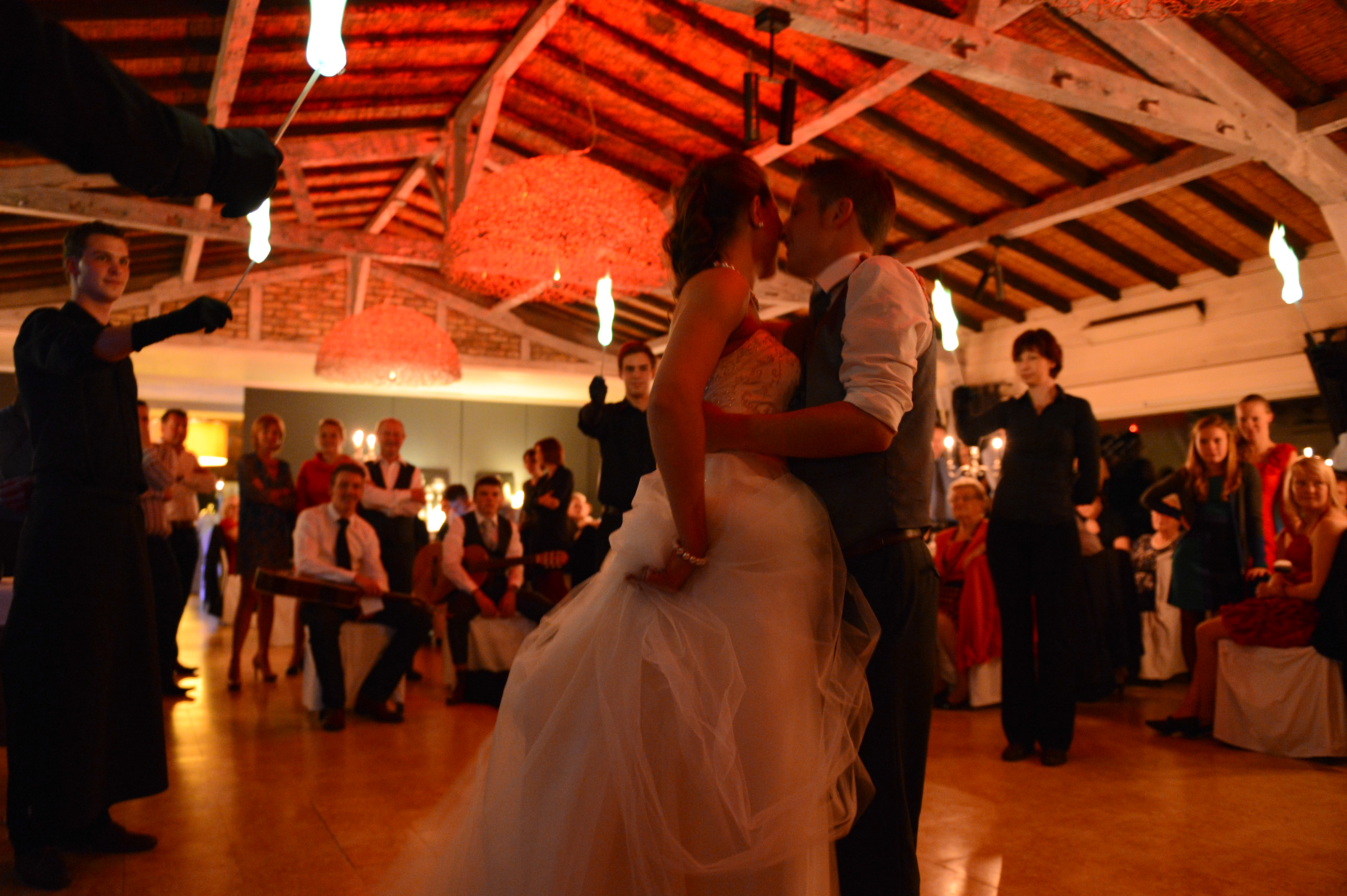 The bride and groom share a kiss on the dance floor while guests watch and a performer holds fire.