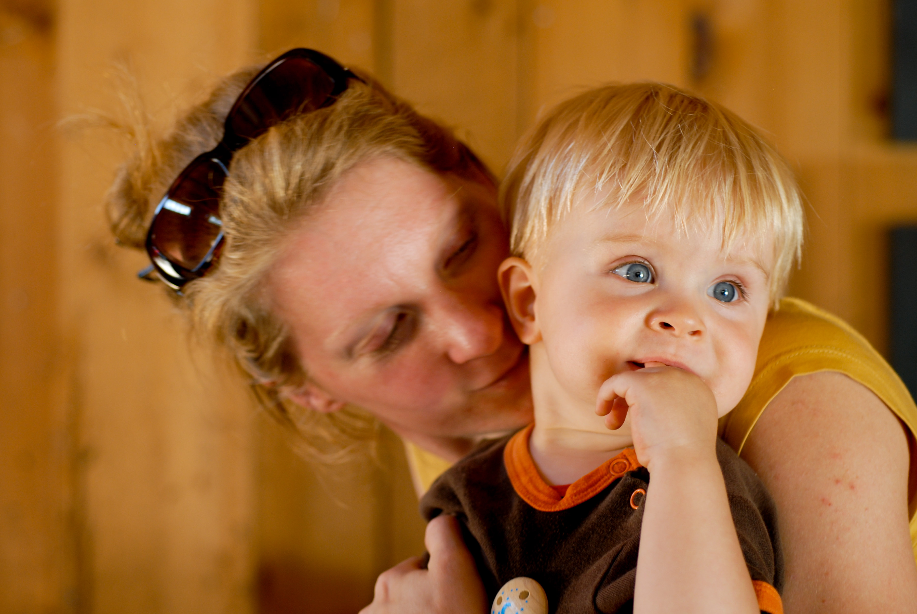 A woman holds a young child close, gently leaning in while the child looks away with a finger in their mouth.