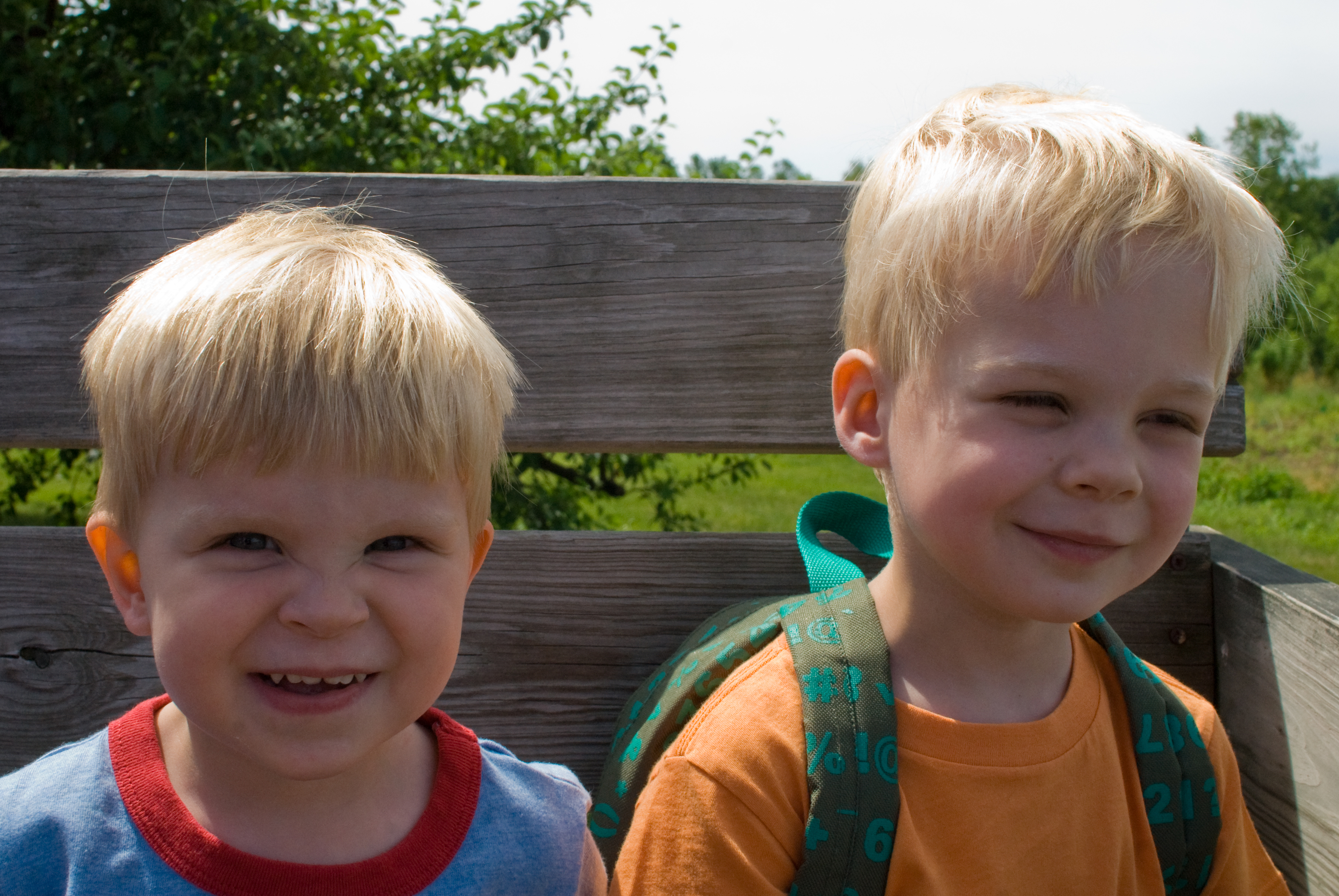 Two young children sitting on a wooden bench outdoors, smiling.