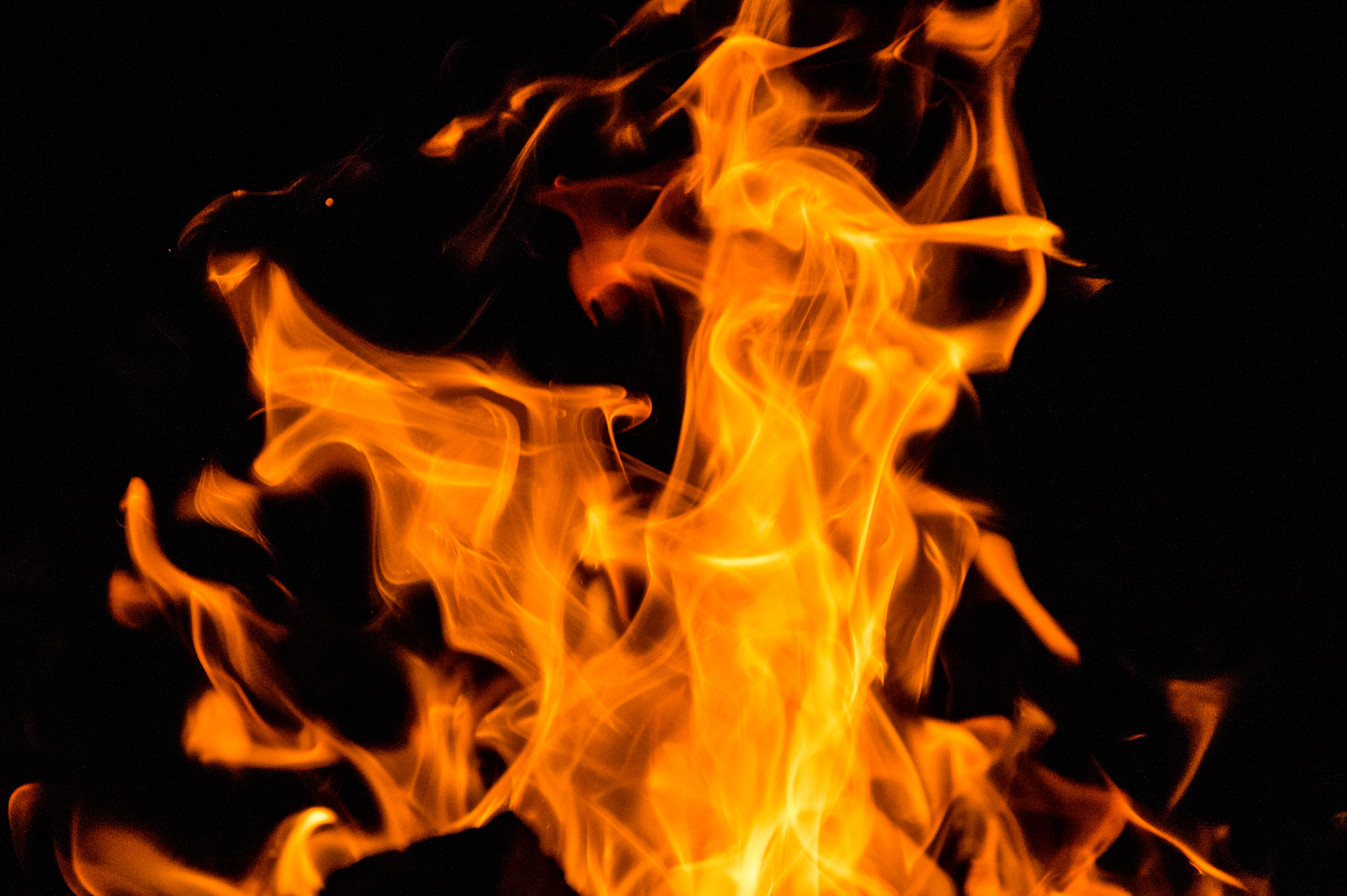 Bright orange flames rise from a campfire at night, creating a warm glow in the darkness.